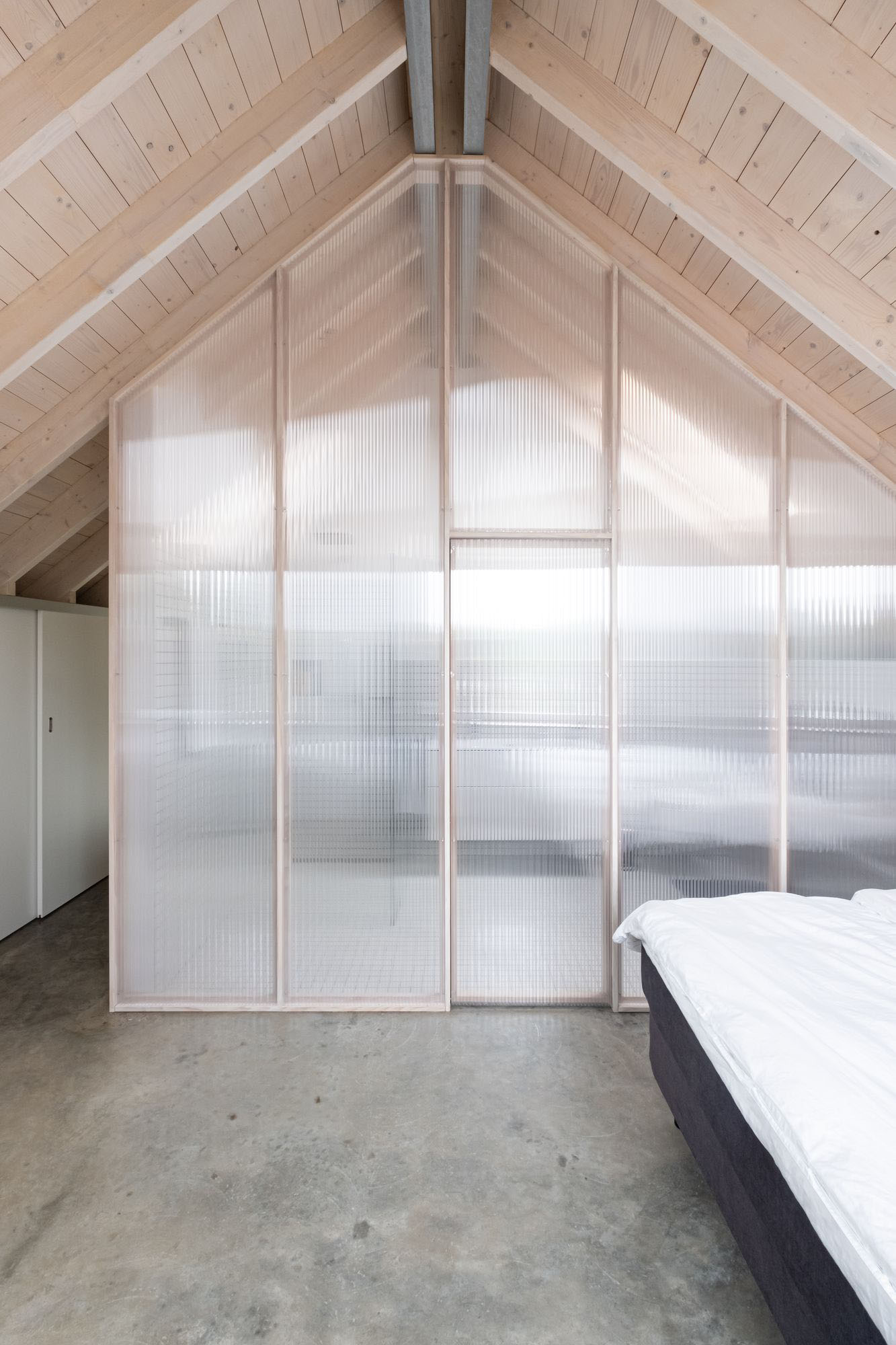 House D6 by Aretz Dürr Architektur — A bedroom mezzanine beneath the timber-framed gable, enclosed by a translucent polycarbonate partition wall with white aluminium mullions.