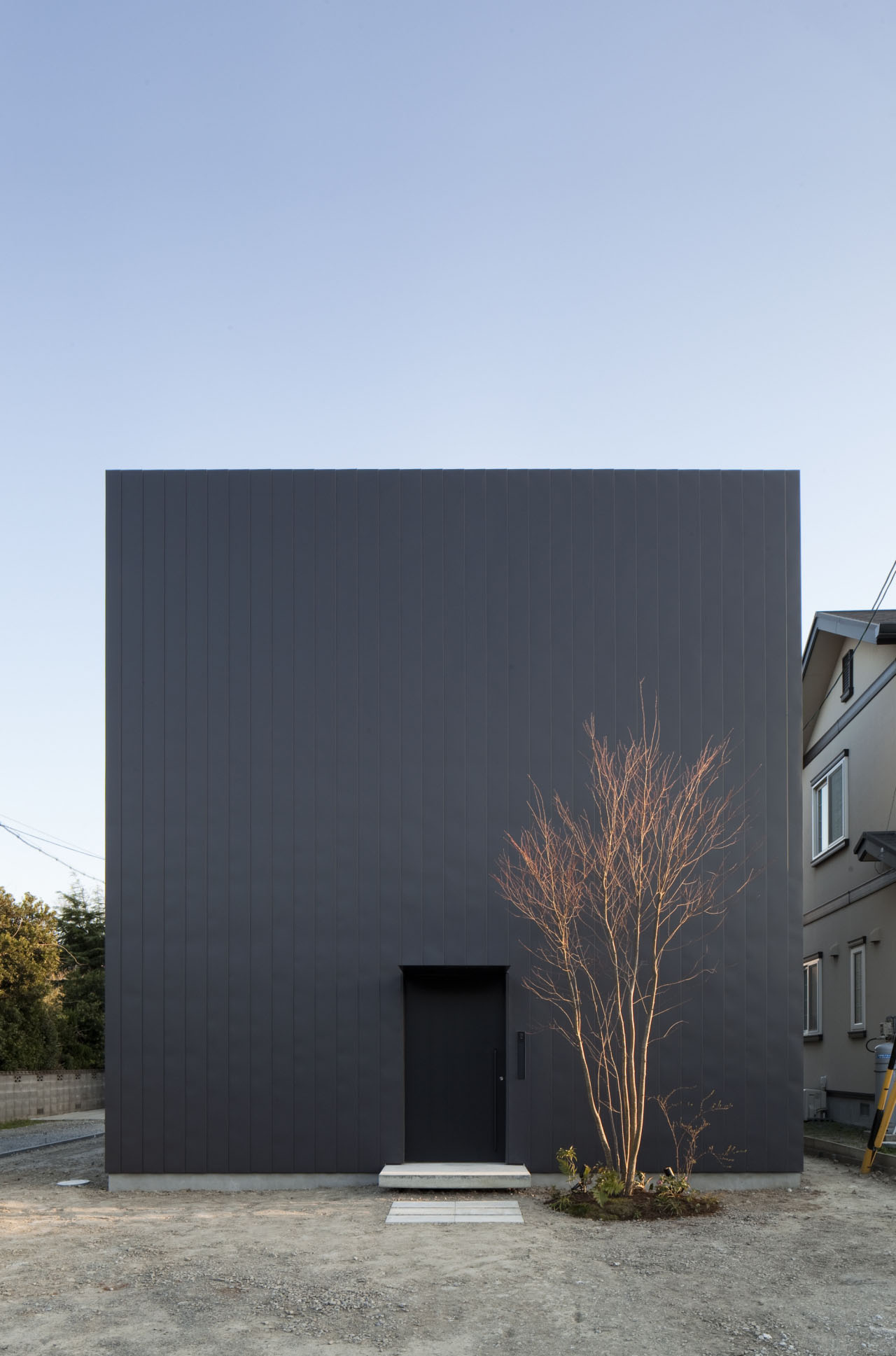 Ant-house by mA-style Architects — The exterior facade presents a monolithic black metal-clad cube, its geometric severity punctuated by a single recessed entrance with white concrete steps.