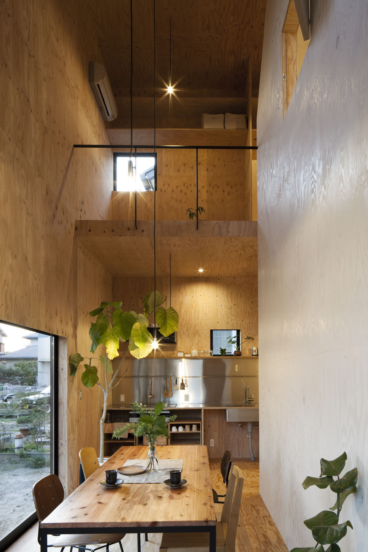 Ant-house by mA-style Architects — A double-height interior volume clad entirely in plywood, revealing the Ant-house's warm timber palette after passage through the windowless black metal facade.