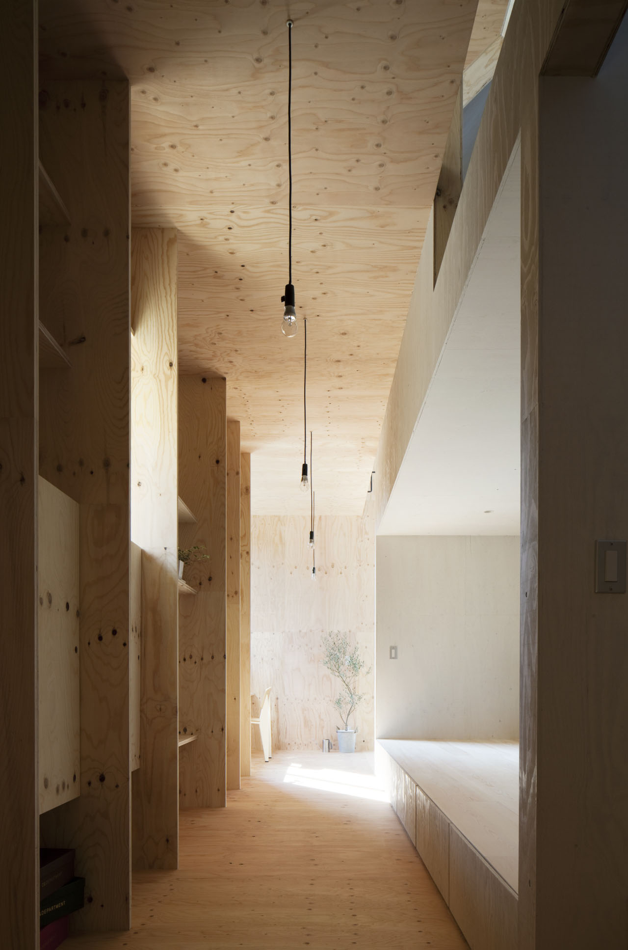 Ant-house by mA-style Architects — A narrow plywood corridor extends toward natural light, its timber ceiling punctuated by three pendant fixtures suspended on black electrical cords.