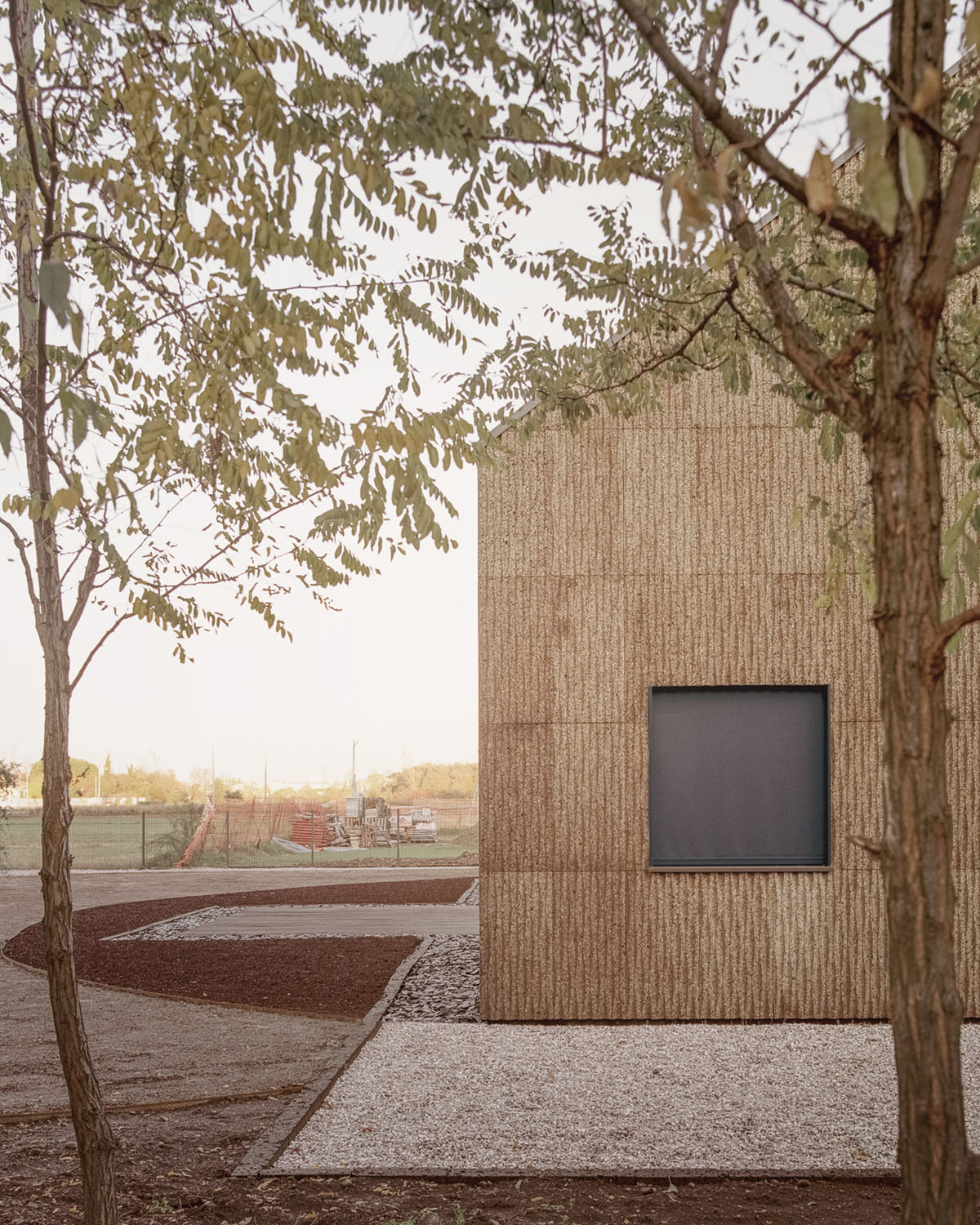 Casa Quattro by LCA Architetti — A single-story timber-clad pavilion emerges from a gravel courtyard, framed by bare deciduous trees in autumn.