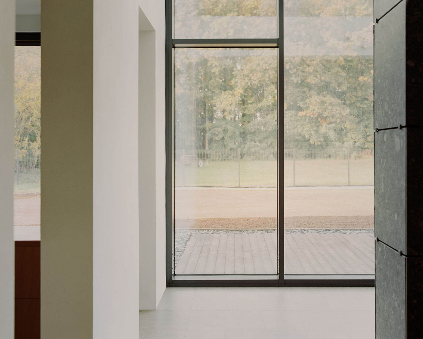 Casa Quattro by LCA Architetti — Interior threshold framing expansive glazed doors with dark metal frames dividing the composition into vertical sections.