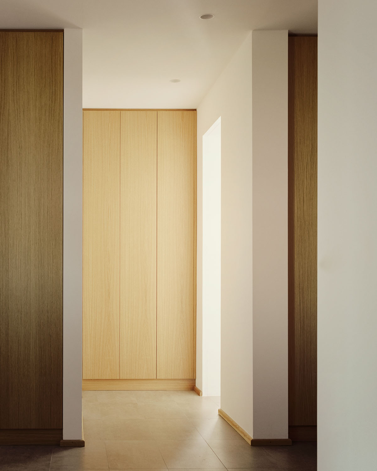 Casa Quattro by LCA Architetti — A passage framed by white-rendered walls and wooden doors, revealing a light-filled room beyond.