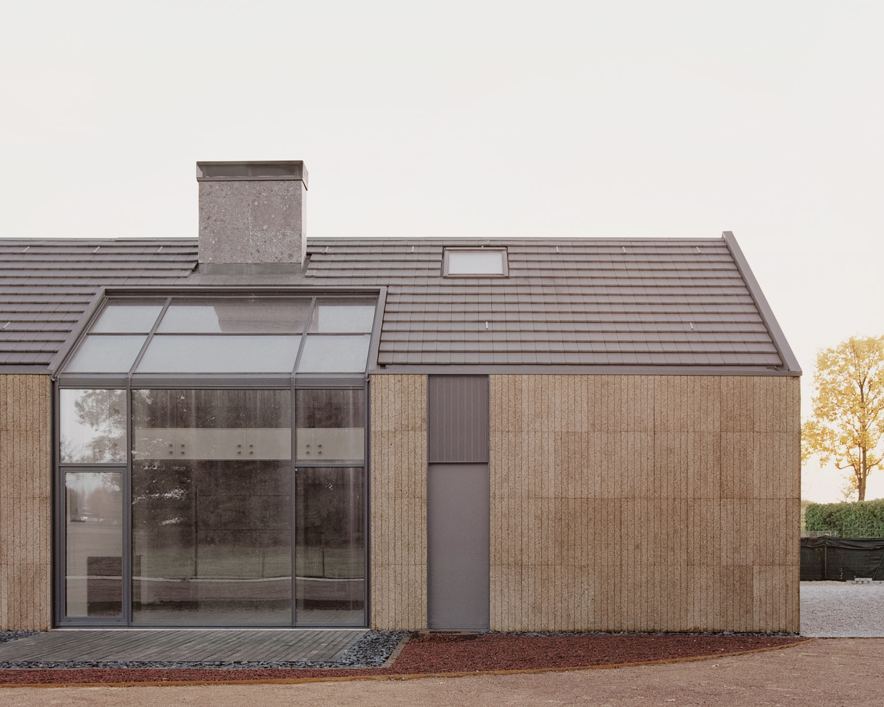 Casa Quattro by LCA Architetti — Casa Quattro's front elevation presents a compact residential volume clad entirely in cork panels with visible horizontal mortar joints and subtle 3D...