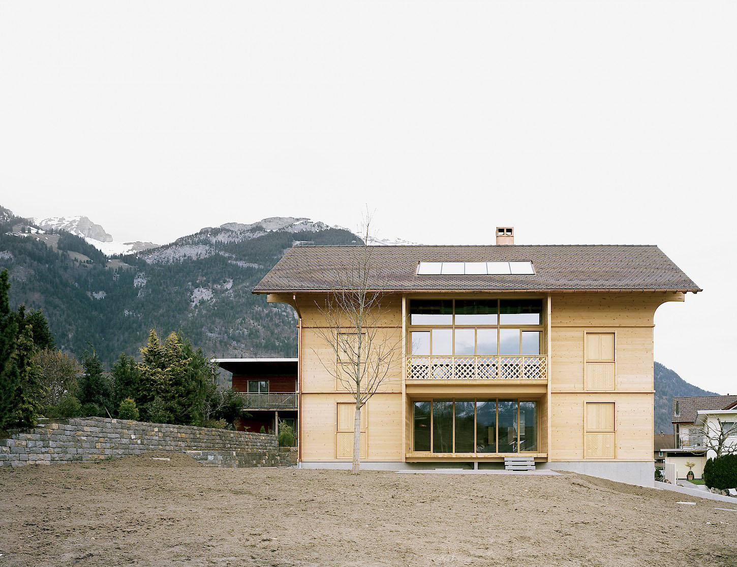 House K Alpnach by Seilerlinhart — House K Alpnach presents a contemporary timber construction elevated on a white concrete plinth, its light wood-grain cladding organized by regularly spaced...