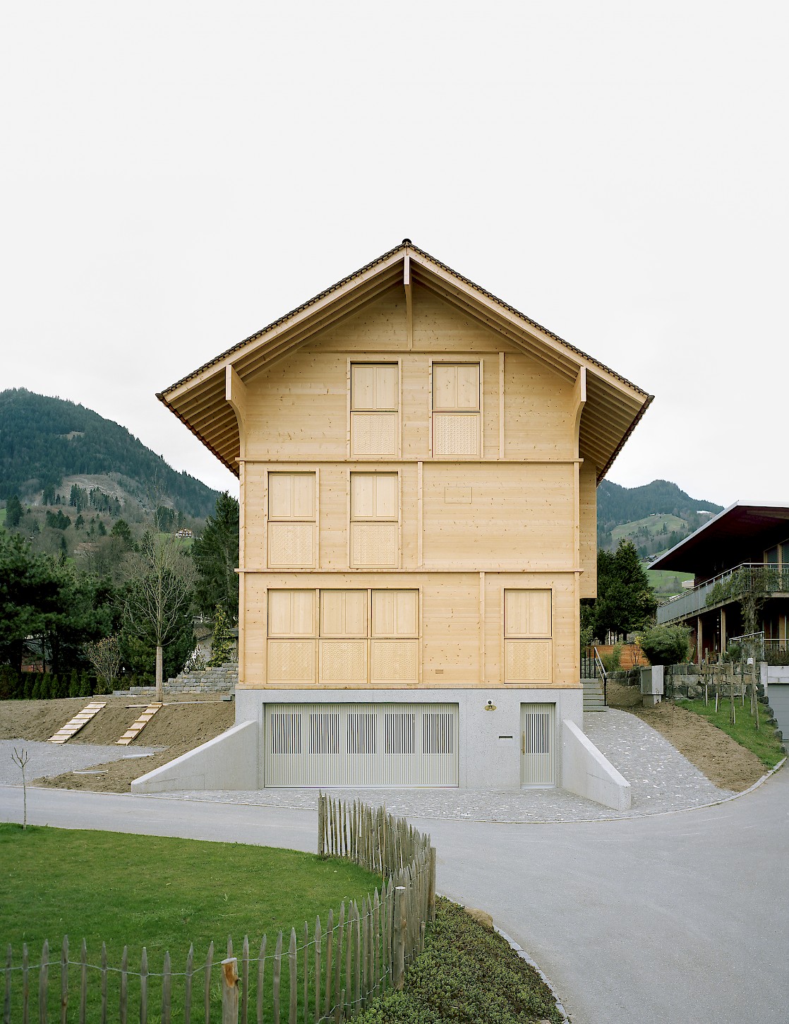 House K Alpnach by Seilerlinhart — House K Alpnach presents a contemporary timber structure elevated on a white concrete plinth, creating a sharp material and chromatic division between...