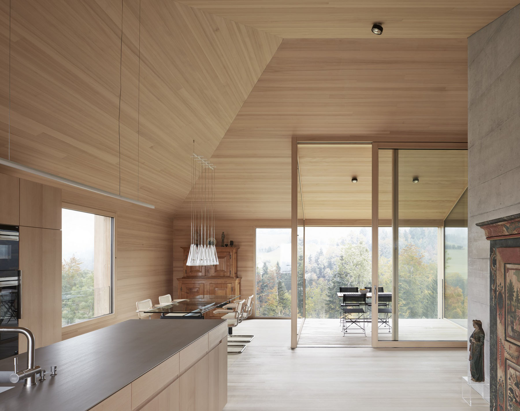 House at the Schopfacker by Bernardo Bader Architects — Open-plan kitchen and dining area unified by continuous horizontal timber slat cladding across walls and coffered ceiling.