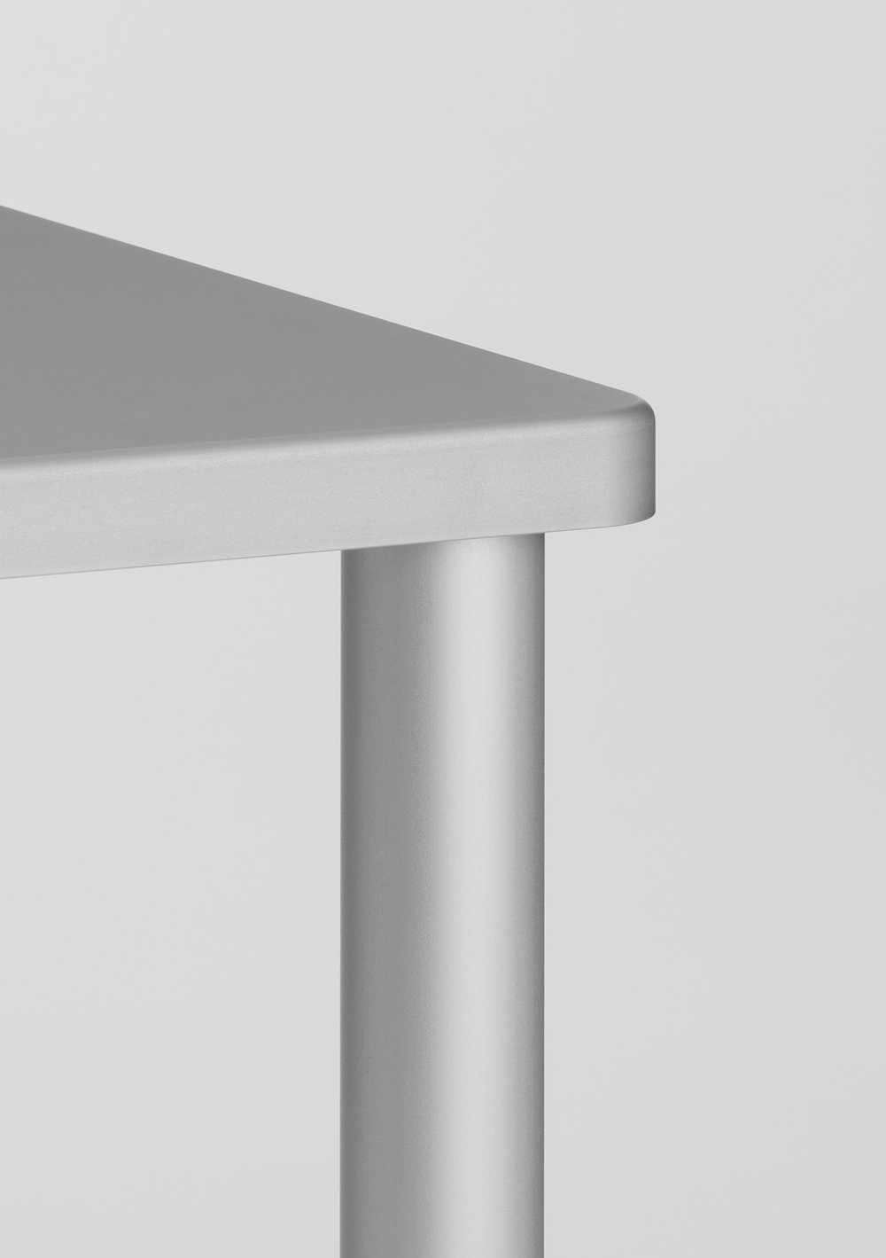 Una Table by Mario Martinez — Close-up detail of Una Table's structural junction, isolating the connection between cast aluminum trapezoid tabletop and cylindrical extruded leg.
