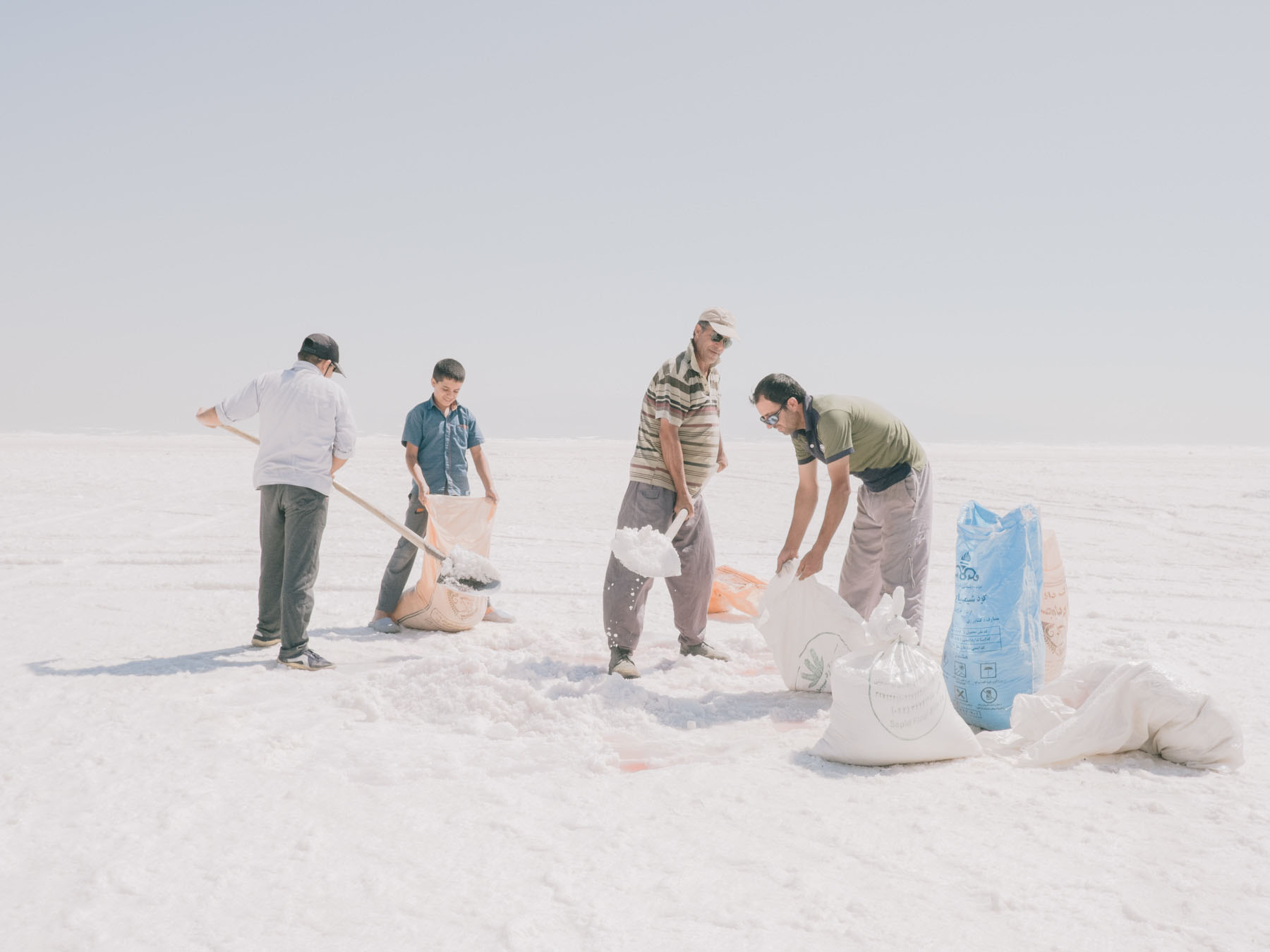 Fading Flamingos by Maximilian Mann — Four figures work across a vast salt flat at Lake Urmia, their forms scattered across the monochromatic landscape.