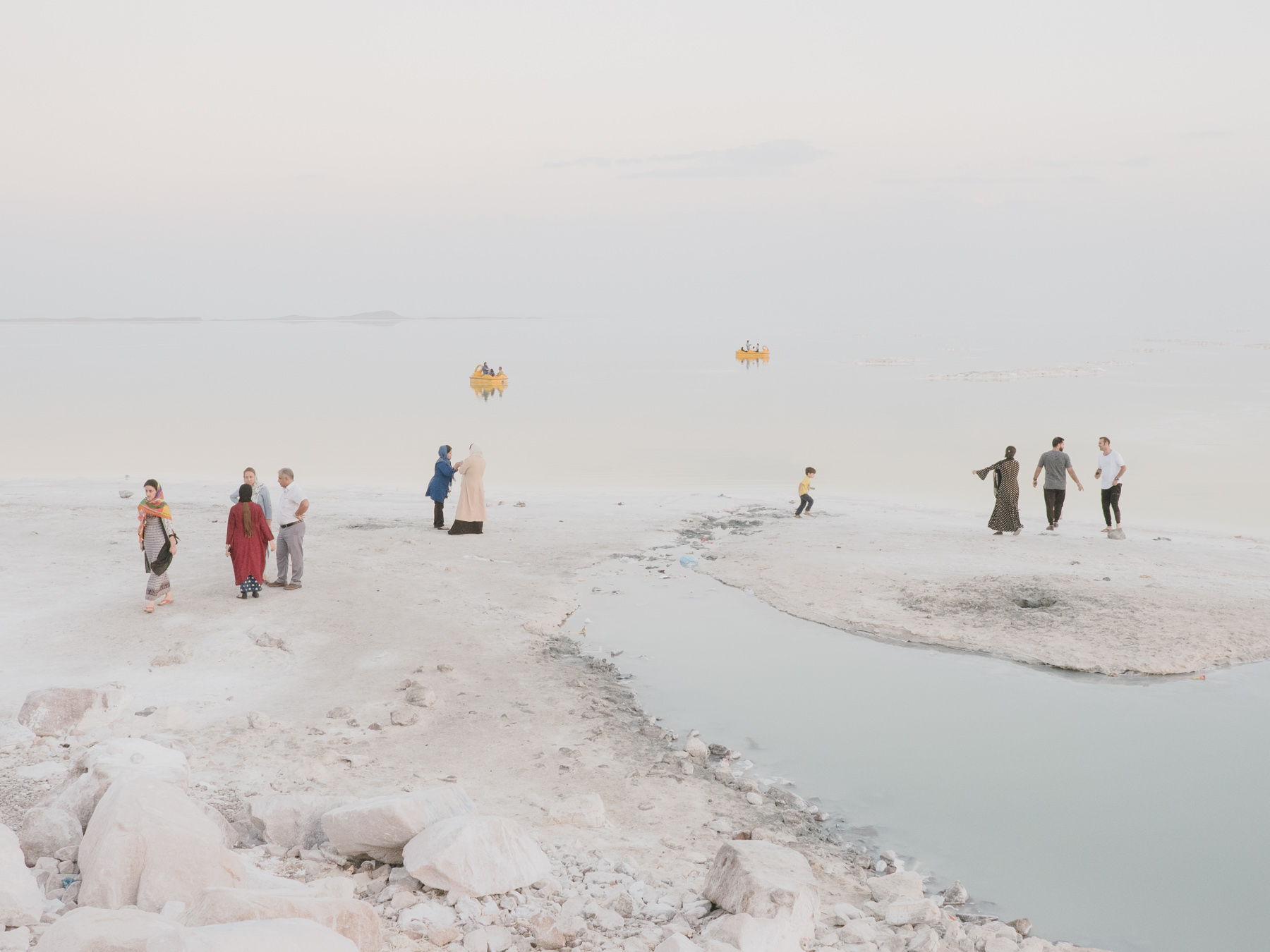 Fading Flamingos by Maximilian Mann — Multiple groups of visitors scattered across the exposed salt flat of Lake Urmia, their figures distributed across the pale grey-beige terrain.