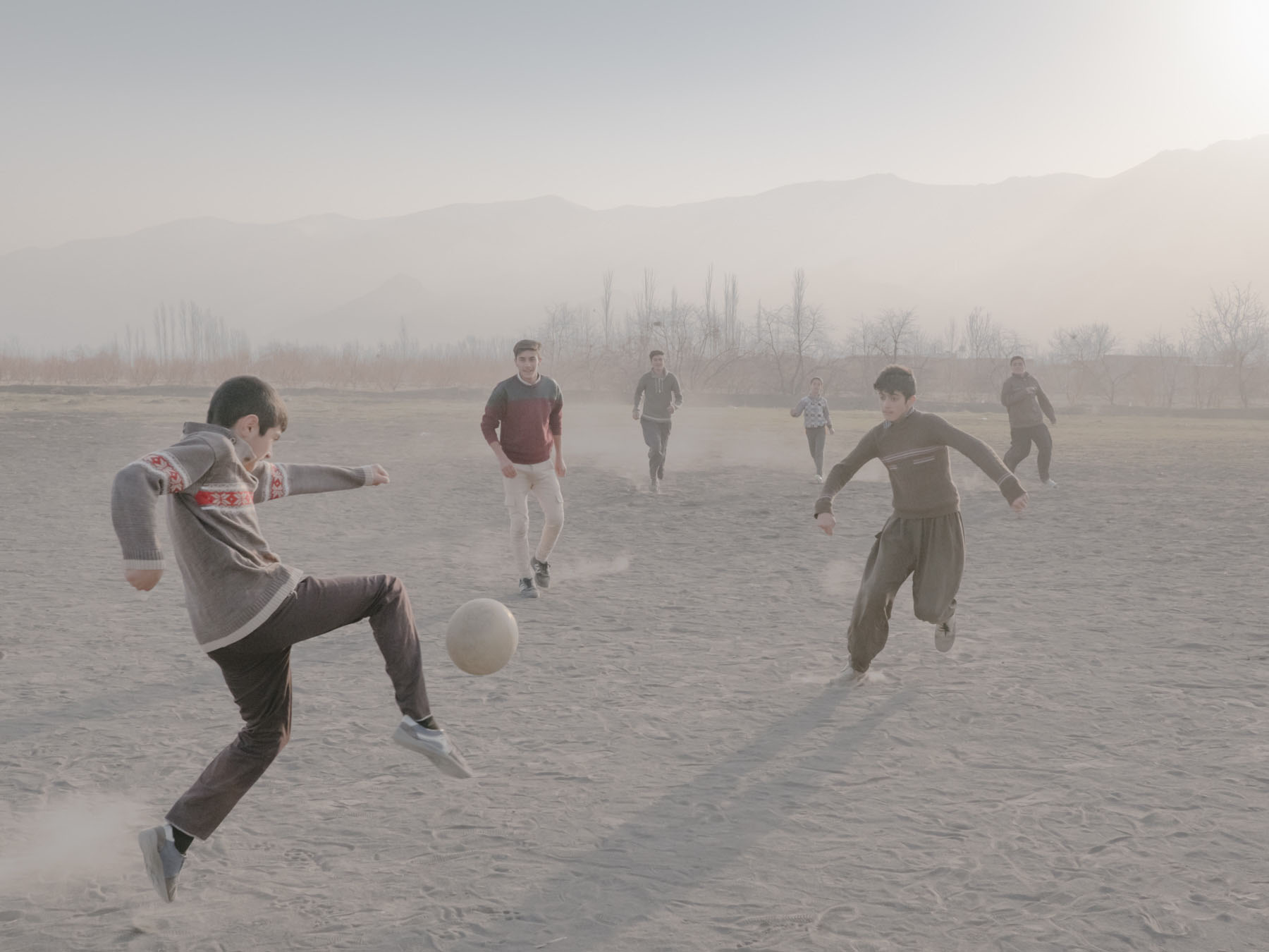 Fading Flamingos by Maximilian Mann — A group of children play football on a vast, dusty salt flat under heavy haze.