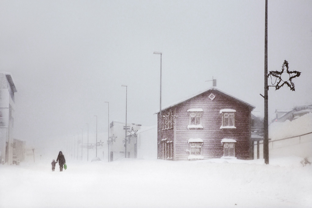 Snjór by Christophe Jacrot — A brick residential structure anchors the composition in heavy snowfall, its pitched roof and multi-pane windows rendered in muted tones against an overcast...