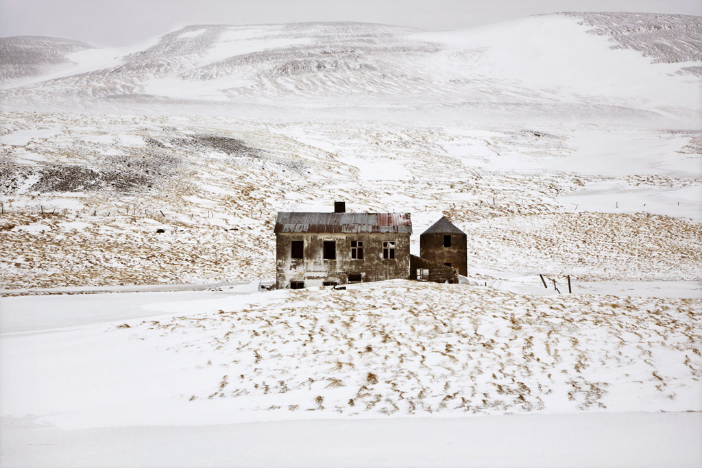 Snjór by Christophe Jacrot — A deteriorated stone structure stands isolated in a snow-covered Icelandic valley, its corrugated metal roof rusted and windows empty.