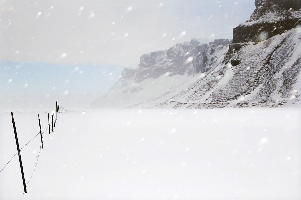 Snjór by Christophe Jacrot — Snow blankets a volcanic landscape in active weather, with precipitation visible across the frame.