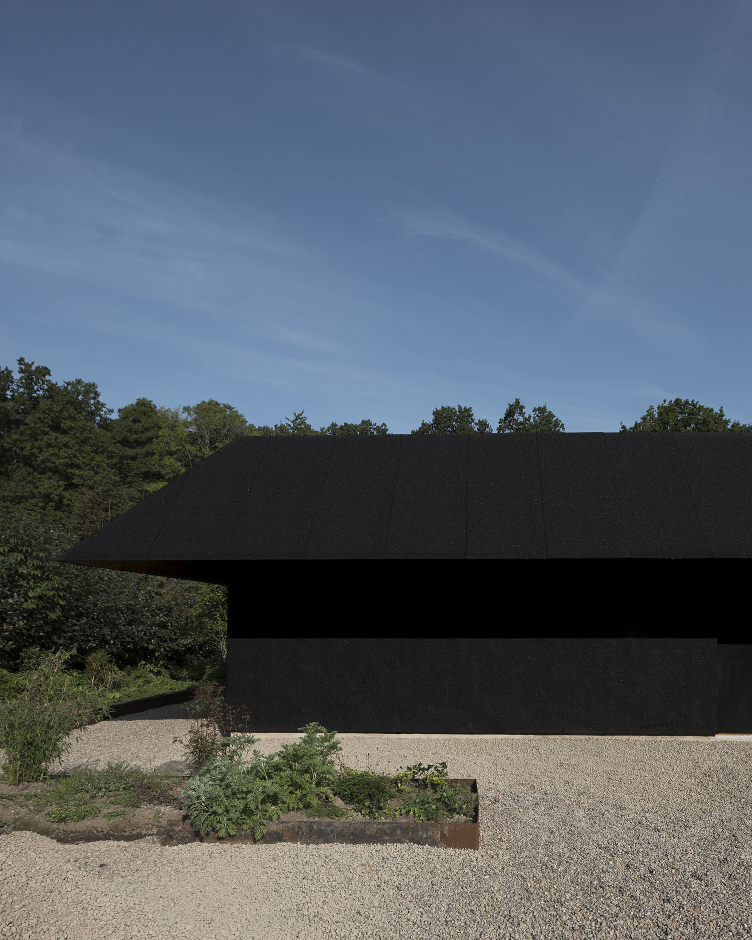 House for Two Artists by Förstberg Ling — The monolithic black exterior reads as a striking counterpoint to the verdant landscape framing it.