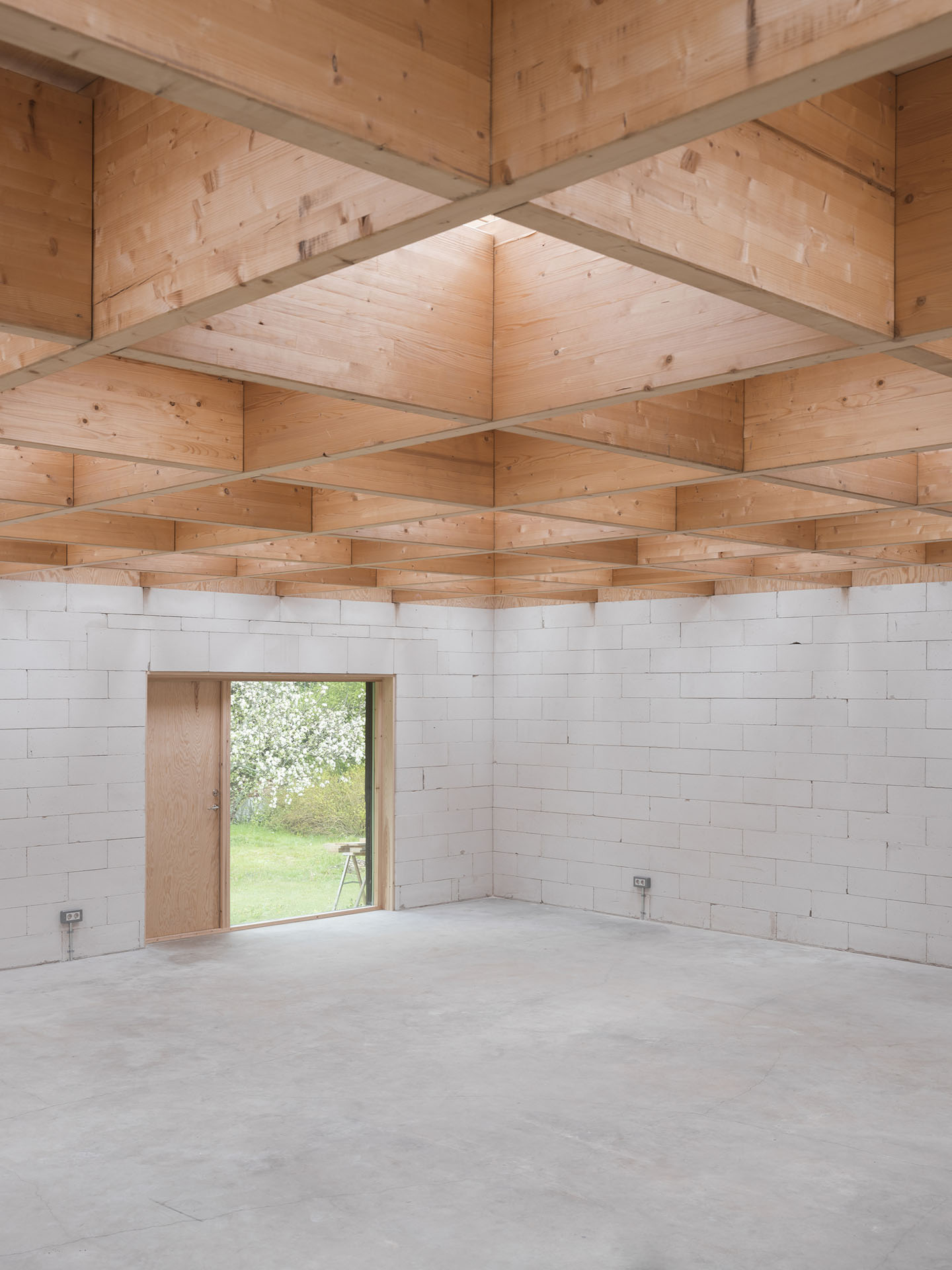 House for Two Artists by Förstberg Ling — Interior view of the atelier space showcasing the coffered ceiling structure of free-spanning glulam beams arranged in a geometric grid, punctuated by...