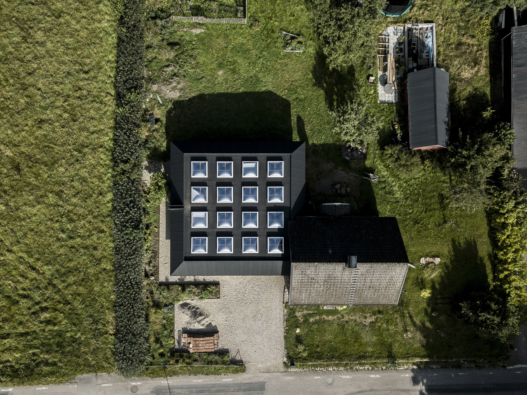 House for Two Artists by Förstberg Ling — Aerial view of House for Two Artists reveals a compact rectilinear volume with a black pitched roof positioned within a densely hedged garden.