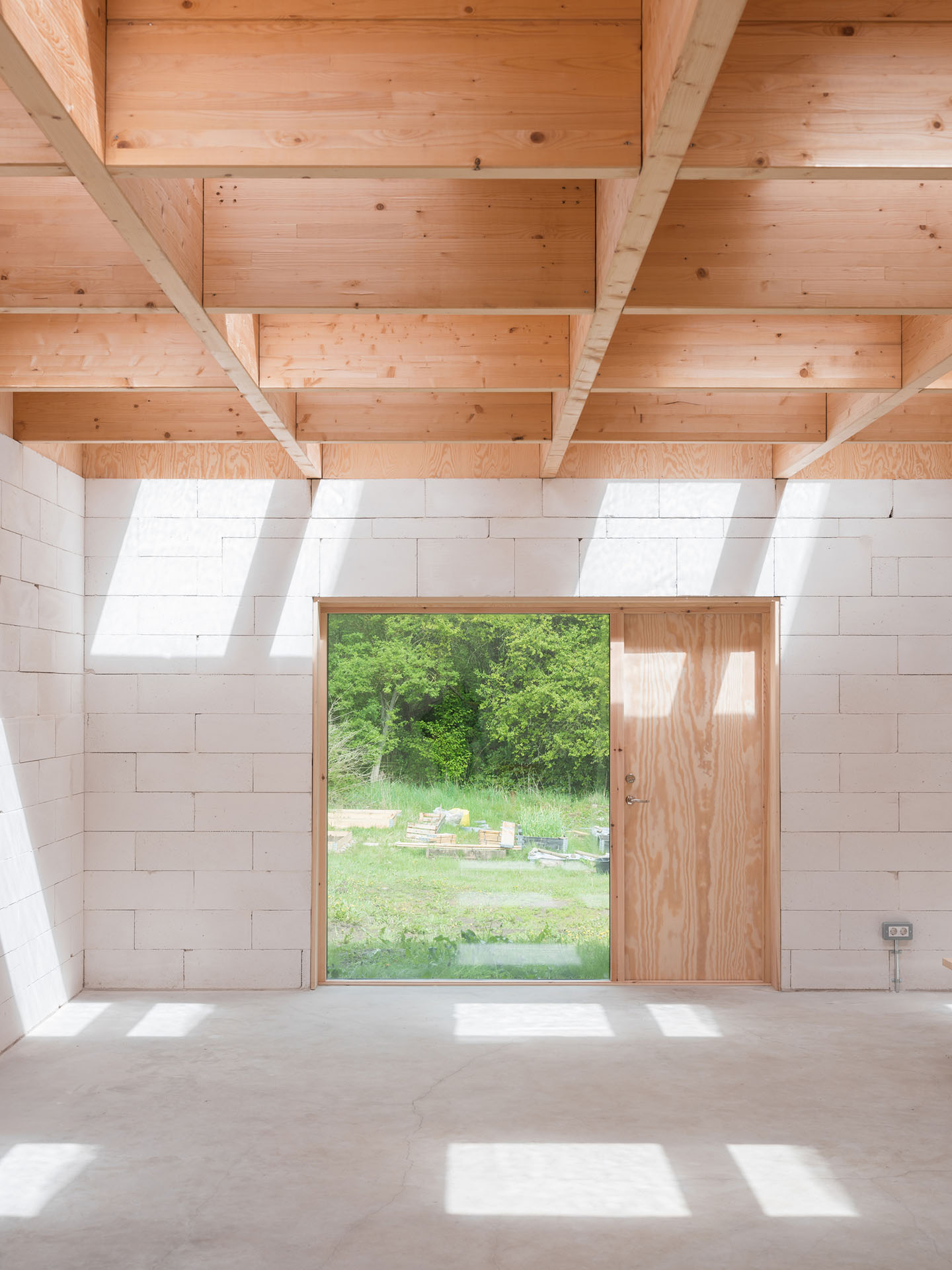 House for Two Artists by Förstberg Ling — An unfinished timber-framed atelier with exposed glulam beams arranged in a coffered grid overhead, punctuated by sixteen skylights.