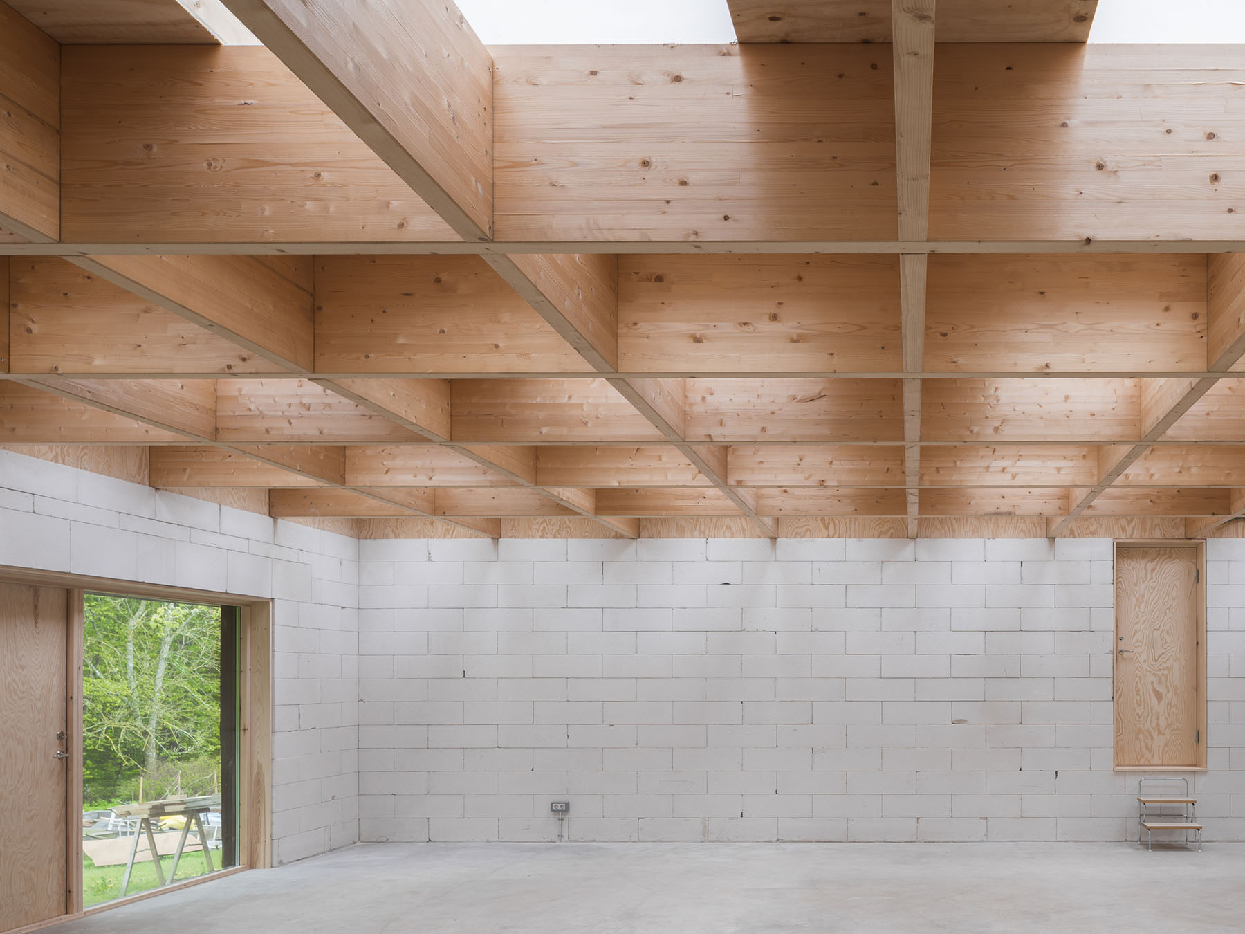 House for Two Artists by Förstberg Ling — An expansive atelier interior defined by a coffered timber ceiling comprising free-spanning glulam beams arranged in a regular grid, punctuated by sixteen...