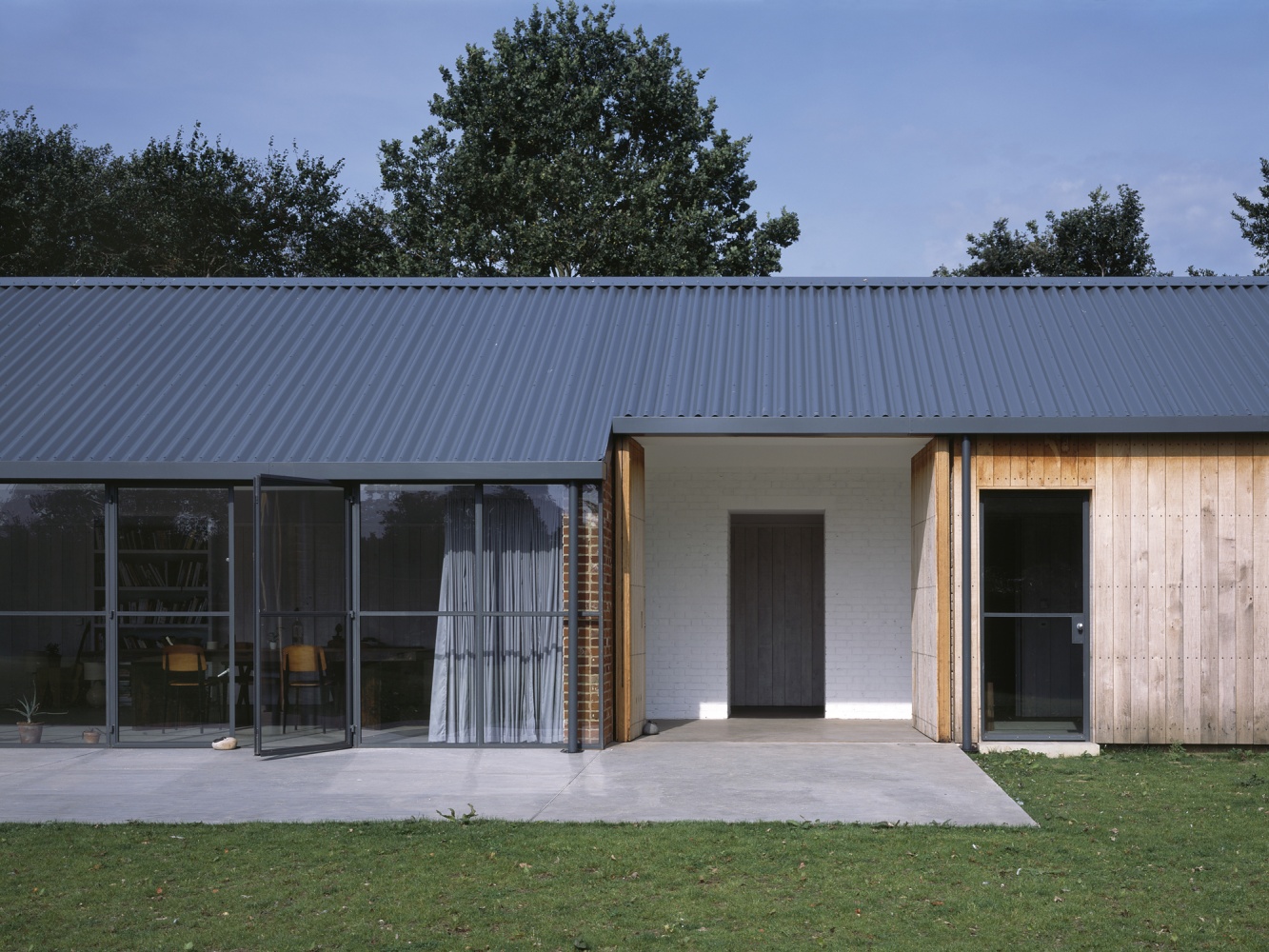 Stable Acre House by David Kohn — The south-facing elevation of Stable Acre House presents a tripartite composition across the rendered concrete plinth.