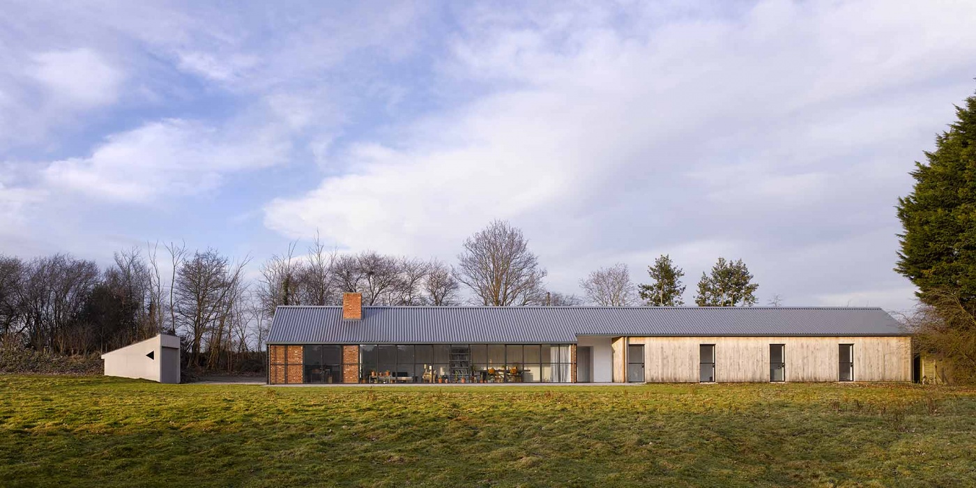 Stable Acre House by David Kohn — Stable Acre House extends as a linear composition across the Norfolk landscape, its profiled metal roof catching pale winter light in sharp geometric planes.