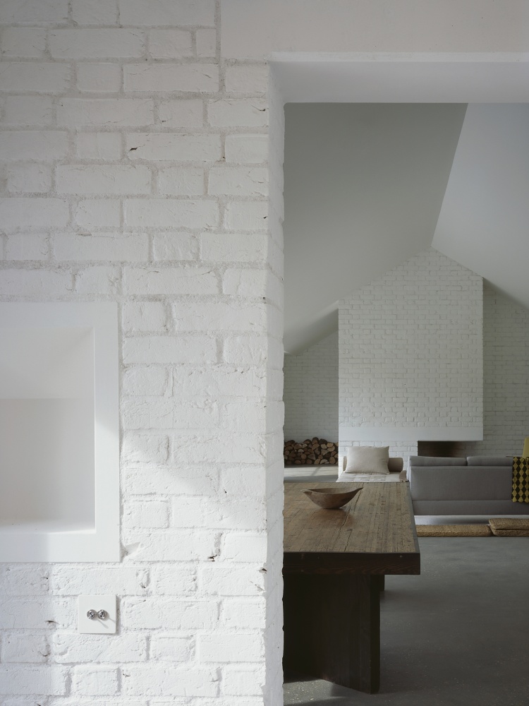 Stable Acre House by David Kohn — Interior view through white-painted brick wall, framing a passage into the living spaces beyond.