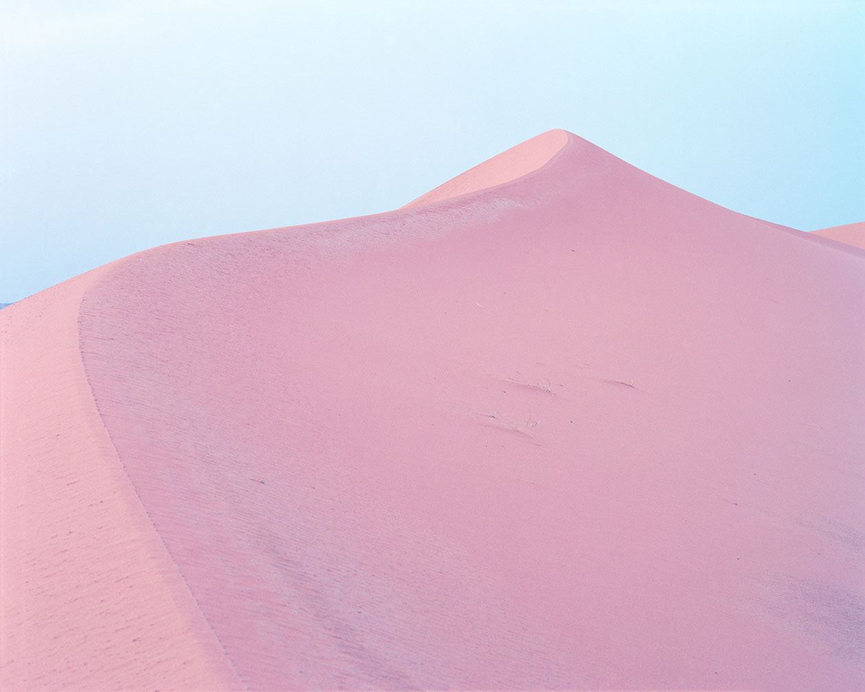 Breathtaking Landscapes by Luca Tombolini — A monolithic sand dune rises against a pale blue sky, its surface marked by wind-carved striations and subtle topographic shifts.