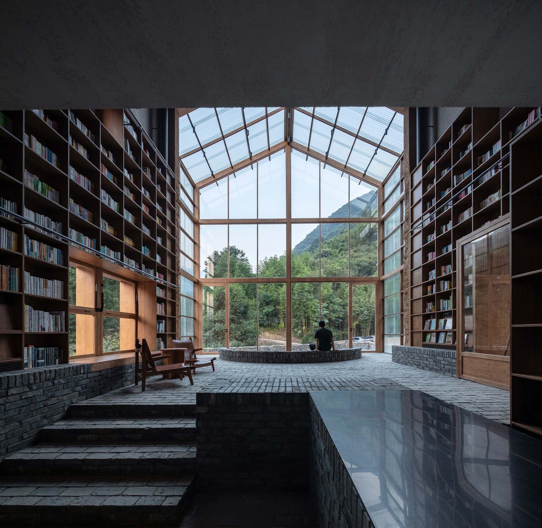 Capsule Hotel and Bookstore in Village Qinglongwu by Atelier tao+c — A timber-framed greenhouse structure houses a double-height interior lined with floor-to-ceiling wooden bookshelves.