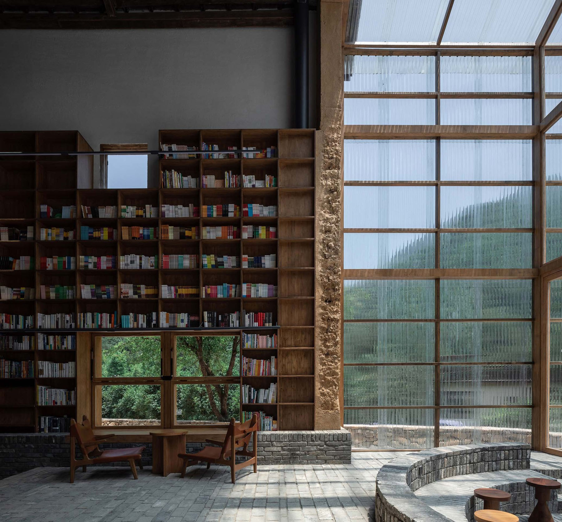 Capsule Hotel and Bookstore in Village Qinglongwu by Atelier tao+c — A timber-framed bookstore interior features floor-to-ceiling wooden shelving units filled with multicolored spines arranged across the left wall.