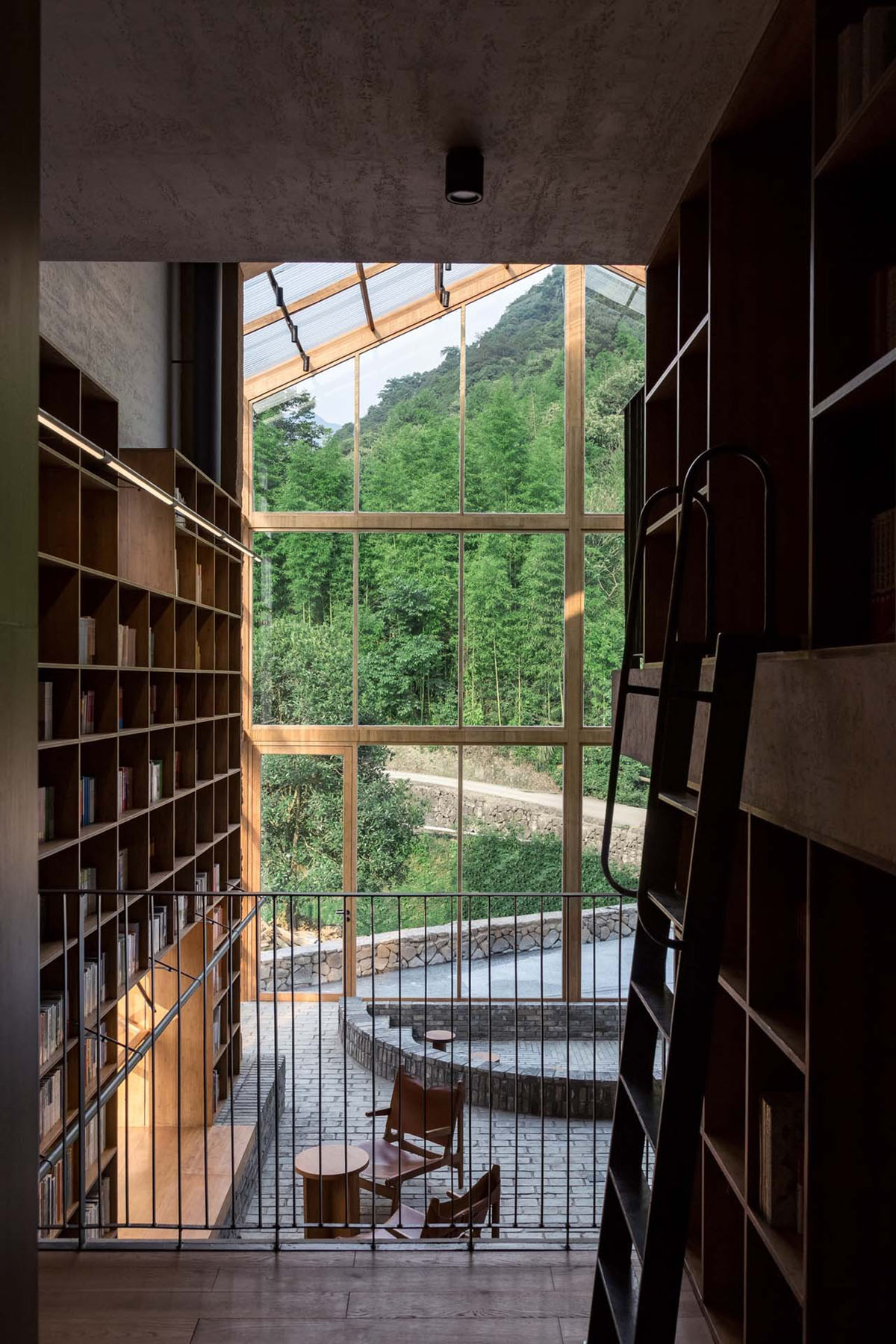 Capsule Hotel and Bookstore in Village Qinglongwu by Atelier tao+c — Interior view through timber-framed glazing looking from a wood-lined corridor toward a cantilevered deck.