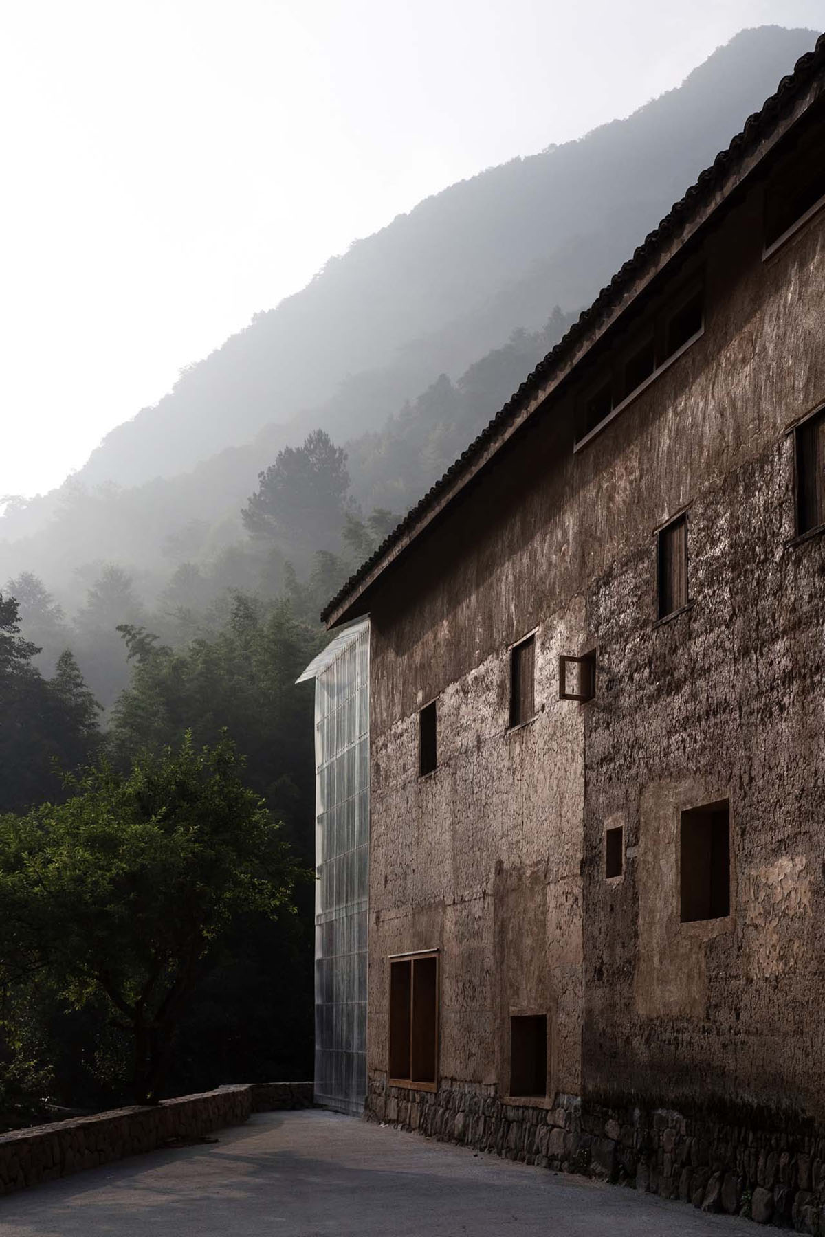 Capsule Hotel and Bookstore in Village Qinglongwu by Atelier tao+c — A weathered stone masonry structure anchors a forested mountainside in Zhejiang.