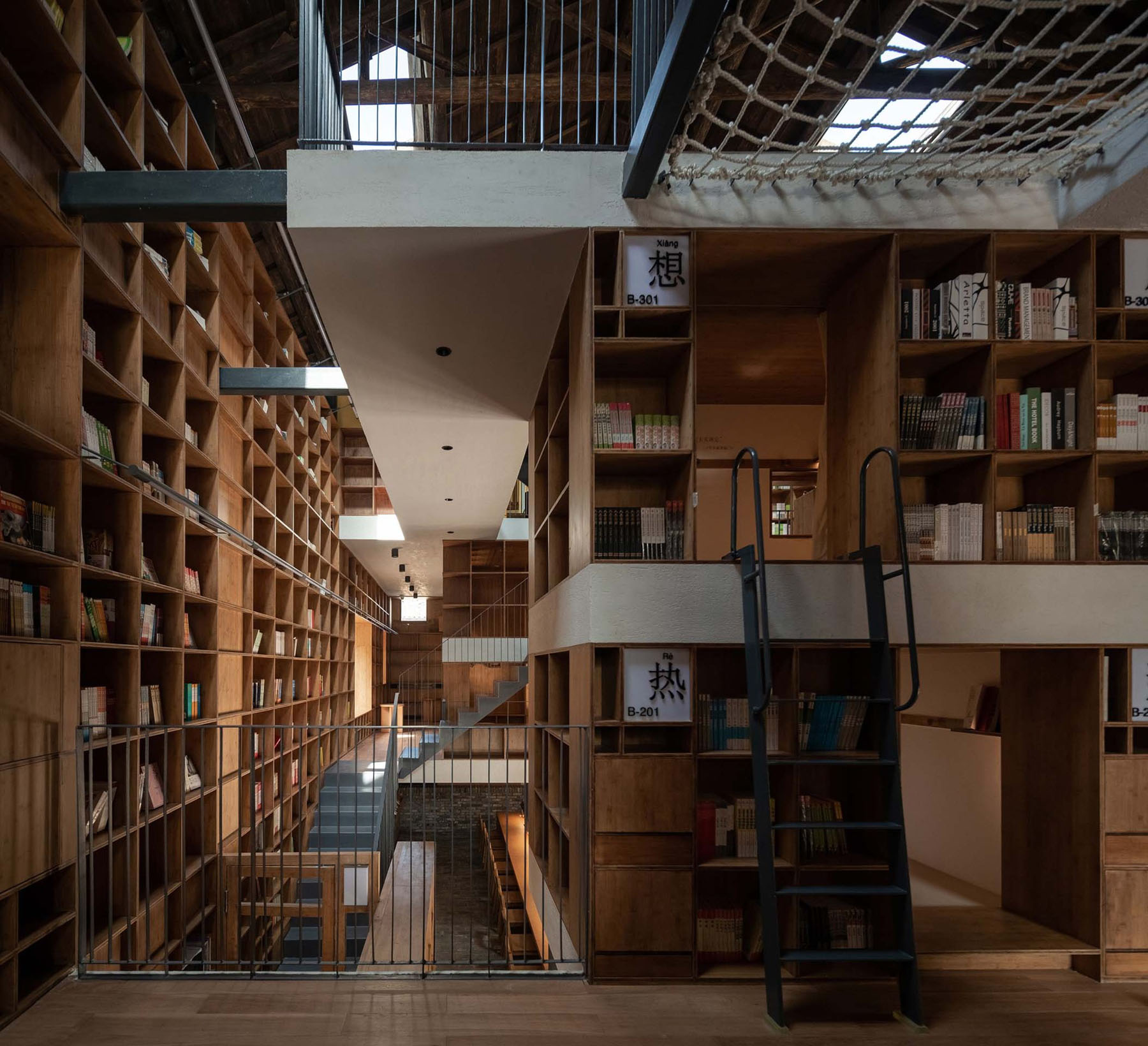 Capsule Hotel and Bookstore in Village Qinglongwu by Atelier tao+c — Interior view of the repurposed capsule hotel and bookstore showing a two-story wooden shelving system organized into modular compartments.