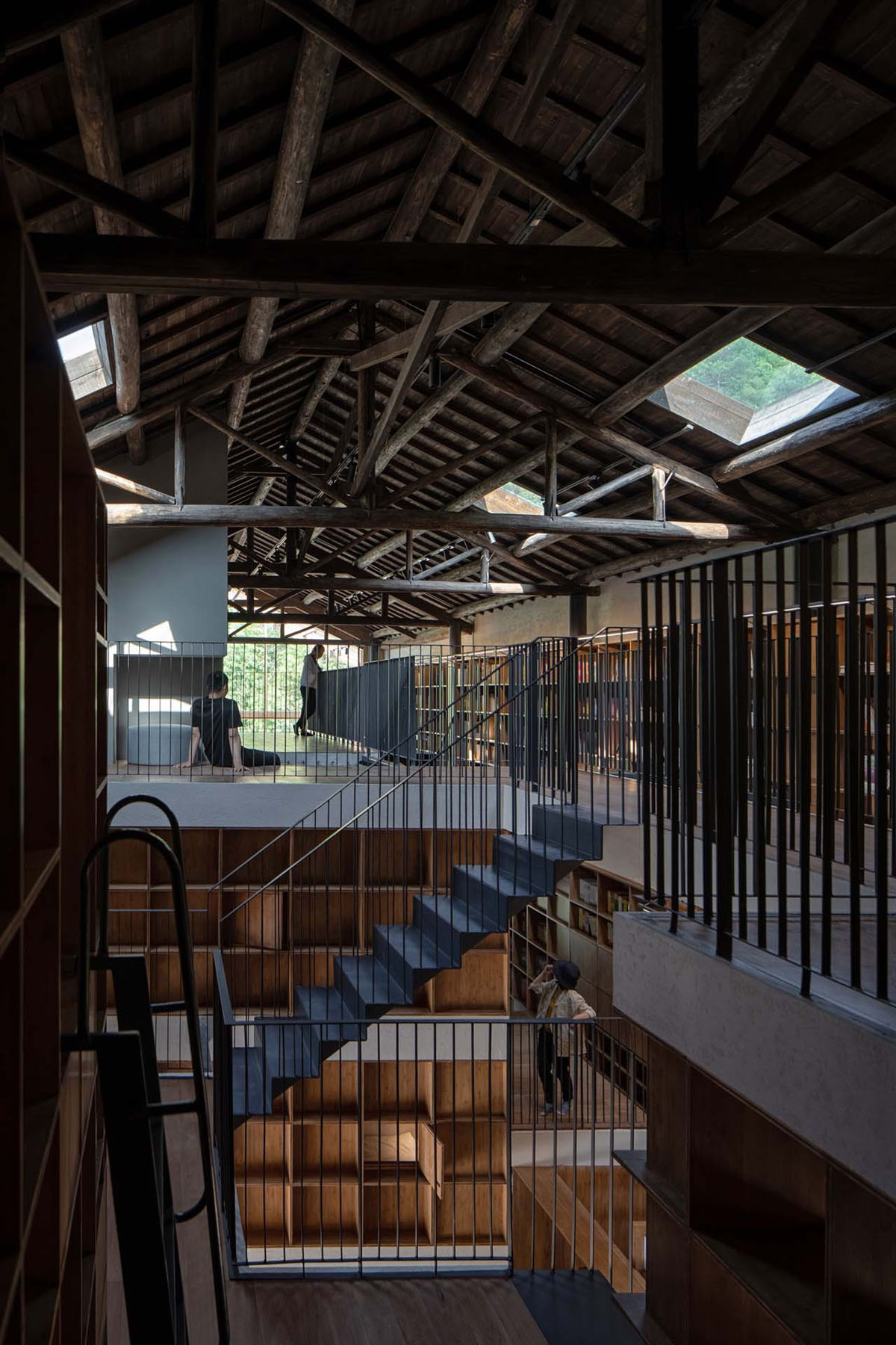 Capsule Hotel and Bookstore in Village Qinglongwu by Atelier tao+c — Interior view of multi-level timber structure with exposed wooden roof trusses and beams demonstrating post-and-beam construction.