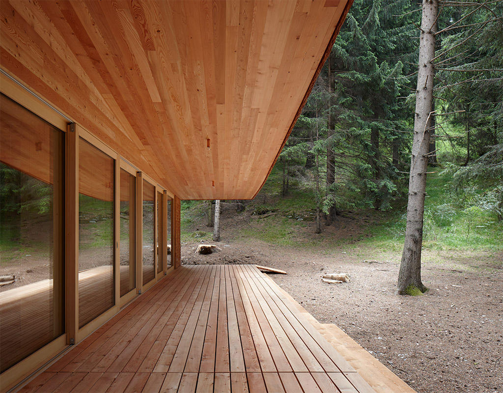 Tegia da vaut forest hut by Gion A. Caminada — The forest hut presents a unified cedar-shingle facade in warm rust-orange tones, with a steeply pitched roof creating a pronounced gable silhouette.