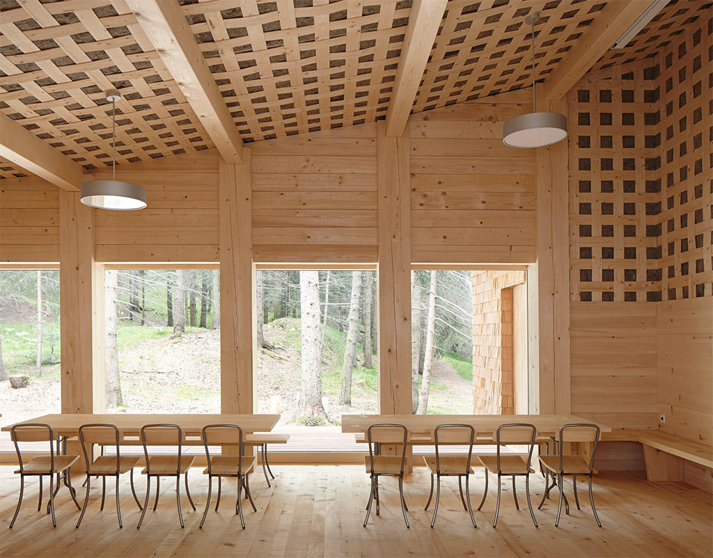 Tegia da vaut forest hut by Gion A. Caminada — Interior view of the forest hut showing the double-height timber-lined space with latticed ceiling panels that filter natural light across the wood floor.