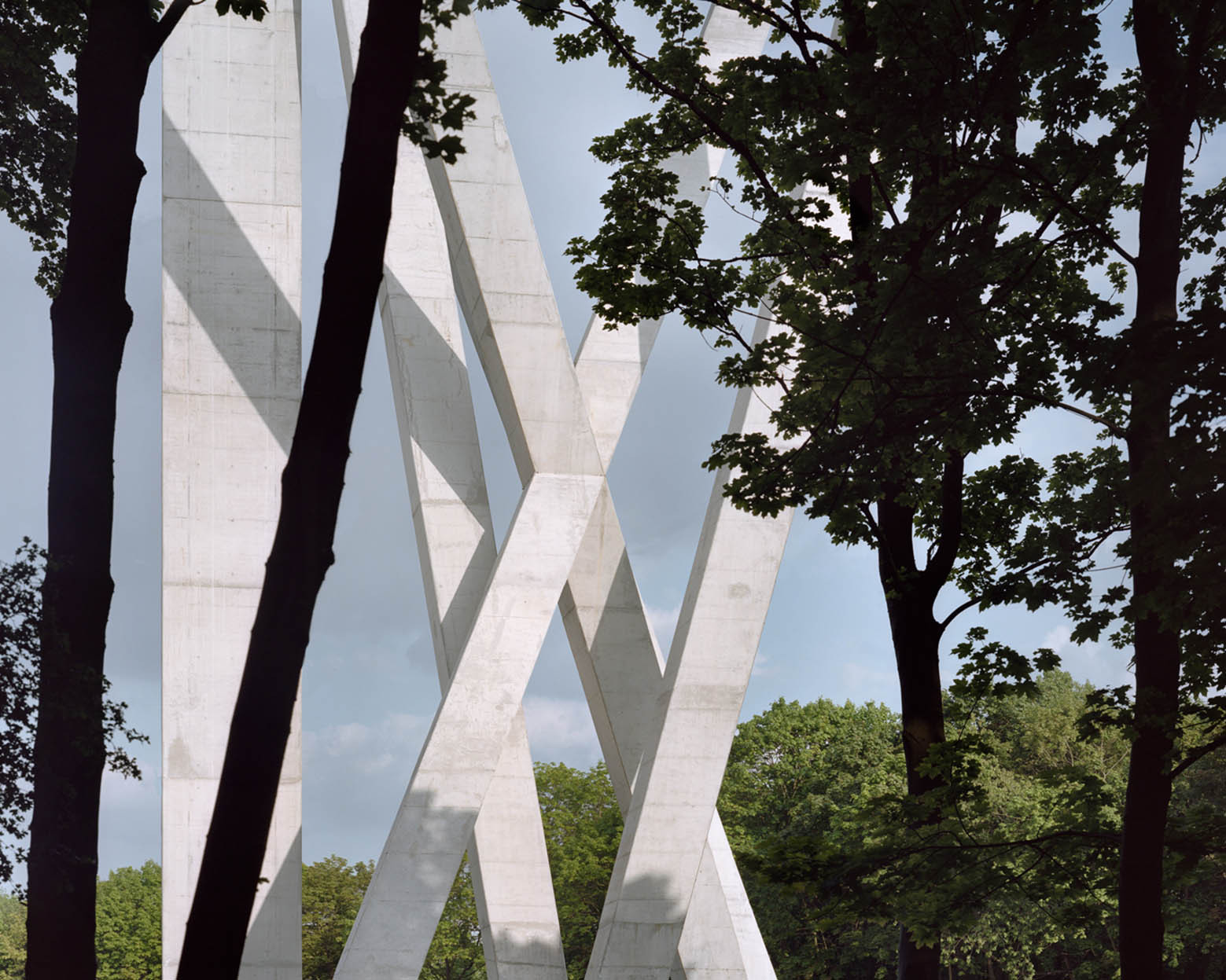 Water Tower by V+ — V+'s water tower rises through a dense forest canopy, its four splayed concrete legs anchoring a monolithic cubic tank elevated high above the surrounding...