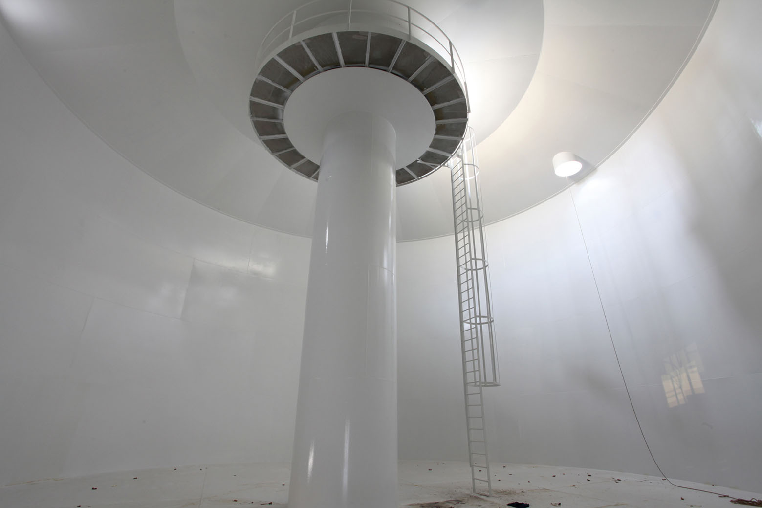 Water Tower by V+ — Interior view of the water tower's central concrete column rising through the tank cavity, photographed from ground level looking upward.