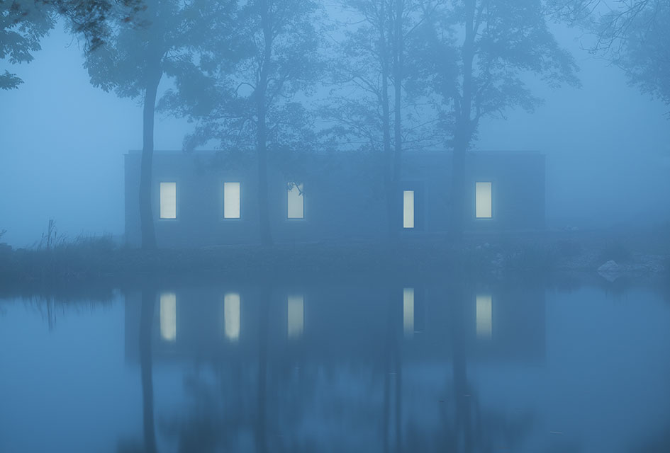 Nový Dvůr Industry by John Pawson — John Pawson's Nový Dvůr monastery workshops materialize through dense fog as a rendered facade with ten flush rectangular windows arranged in two...