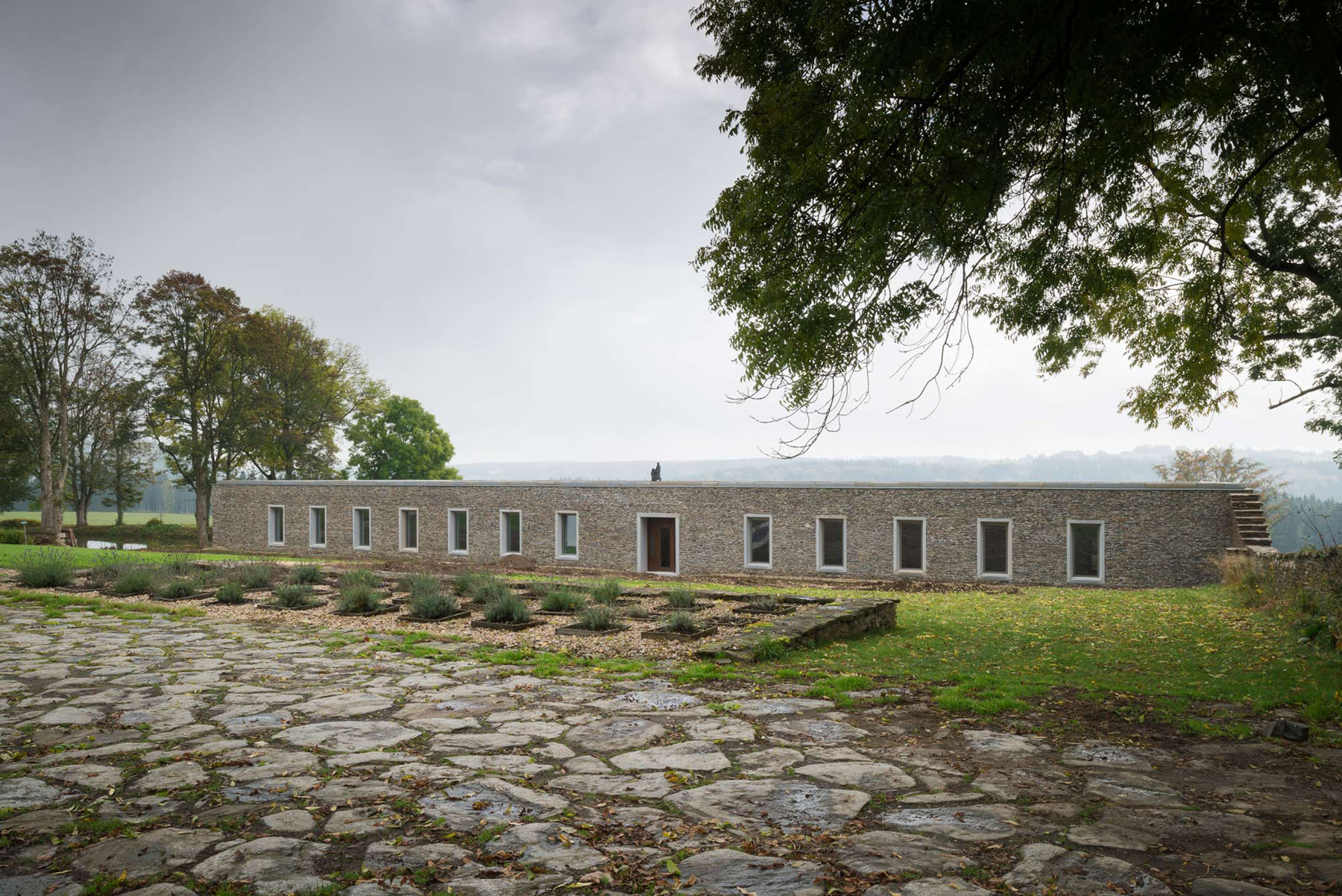 Nový Dvůr Industry by John Pawson — John Pawson's industrial workshop at Nový Dvůr presents a rendered masonry facade with twelve flush rectangular window openings arranged in strict...