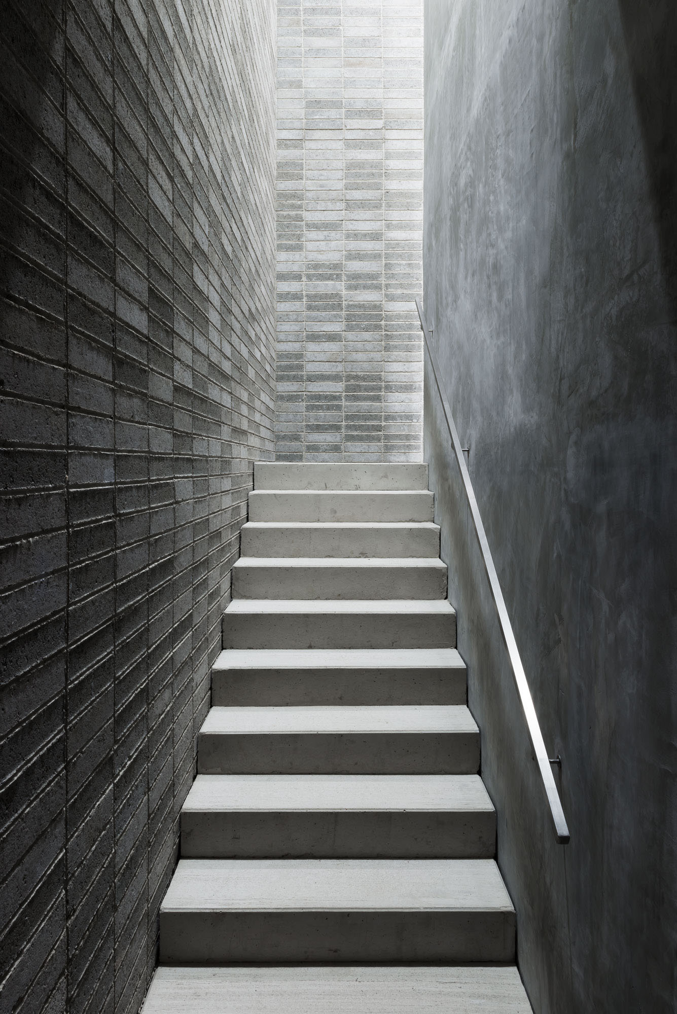 Nový Dvůr Industry by John Pawson — A narrow stairwell ascends between two concrete walls in a recessed passage.