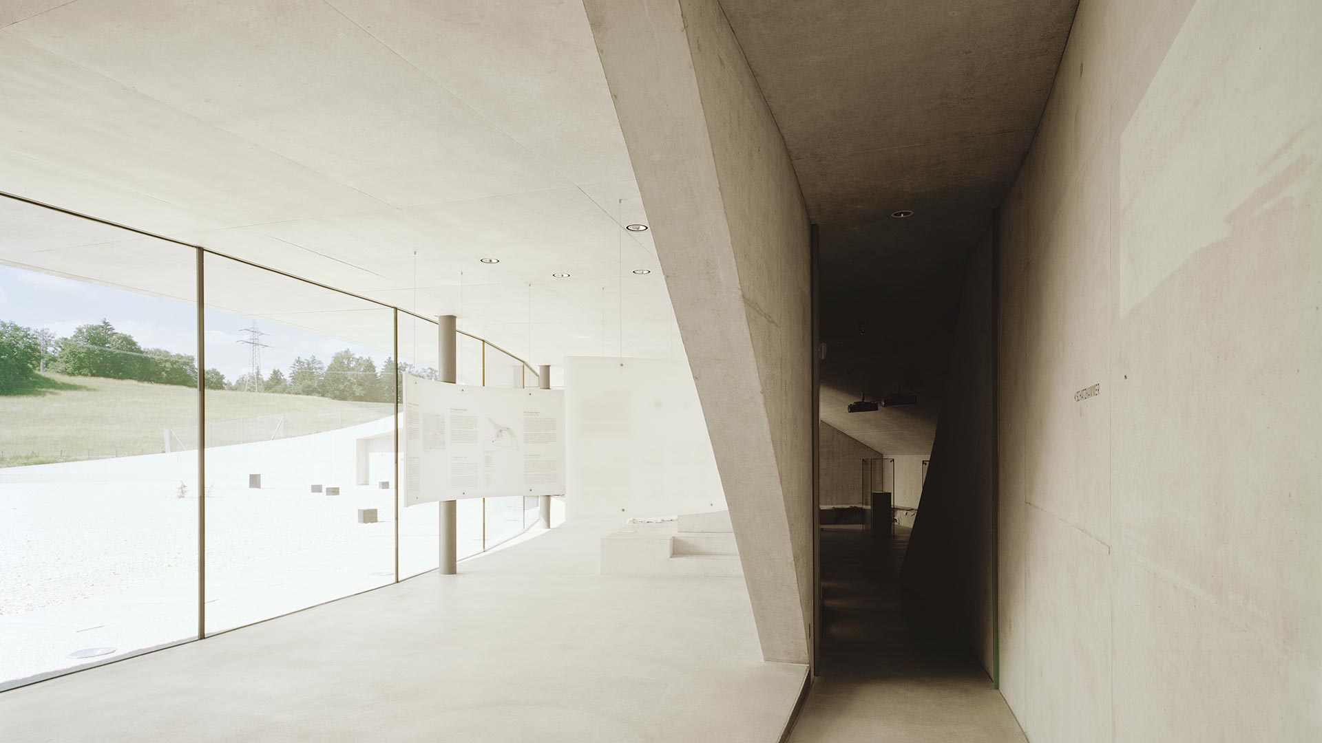 Information Center Archäopark Vogelherd by Ritter Jockisch Architects — A glazed corridor opens onto the courtyard-facing facade of the Information Center, where a continuous glass wall frames views of the Vogelherd hill beyond.