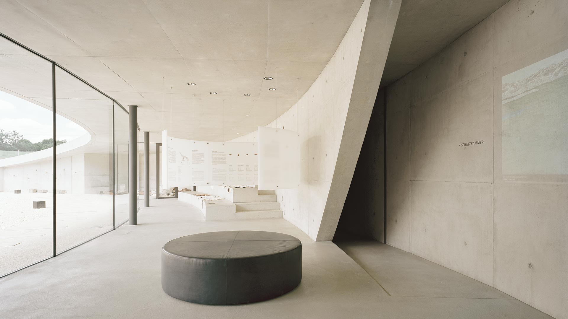 Information Center Archäopark Vogelherd by Ritter Jockisch Architects — The foyer interior presents a monolithic concrete environment defined by curving ceiling geometry and robust structural columns.