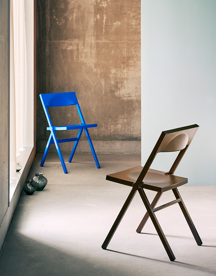 Piana Chair by David Chipperfield — Two molded polypropylene folding chairs demonstrate the Piana's functional design across material and colour contrasts.