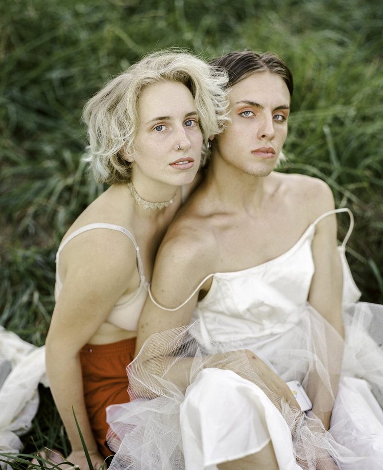 Infinite Tenderness by Peyton Fulford — Two figures positioned in close proximity on grass with green foliage backdrop.