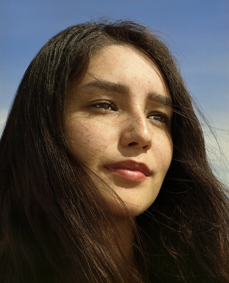Infinite Tenderness by Peyton Fulford — A portrait photograph capturing a woman with long dark hair against a clear blue sky.