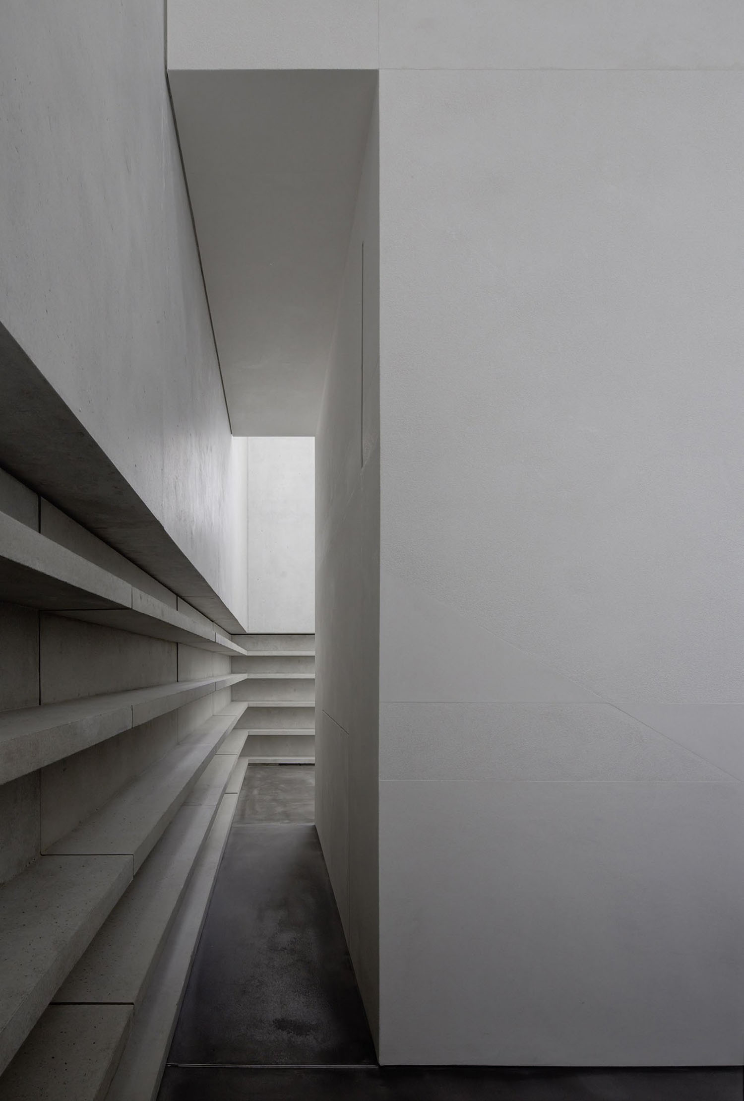 Neue Meisterhäuser Bauhaus Dessau by Bruno Fioretti Marquez — A narrow concrete passage frames stepped internal shelving that descends leftward in uniform horizontal planes.