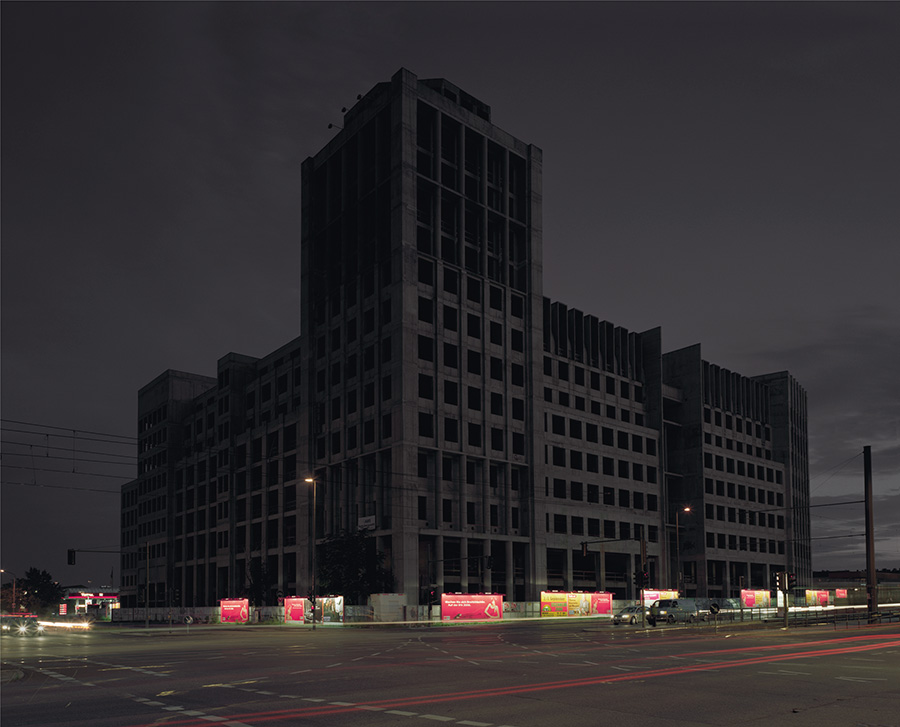 Aftermath by Jörn Vanhöfen — A monolithic mid-century modernist tower block dominates the twilight frame, its concrete facade gridded by rows of recessed windows creating deep shadow...