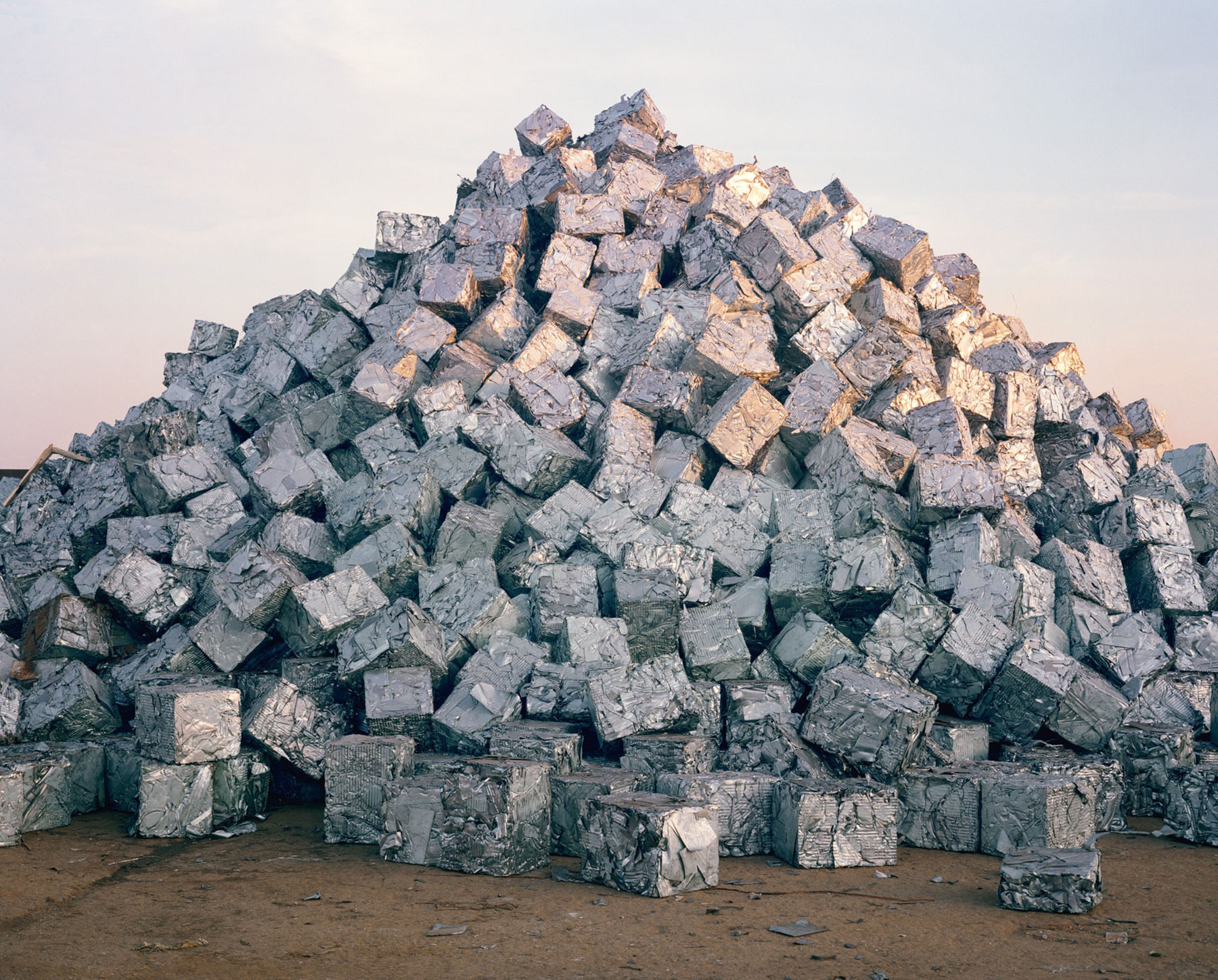 Aftermath by Jörn Vanhöfen — A conical mound of reclaimed concrete blocks rises against an overcast sky, constructed from hundreds of uniform cubic units stacked without mortar or...