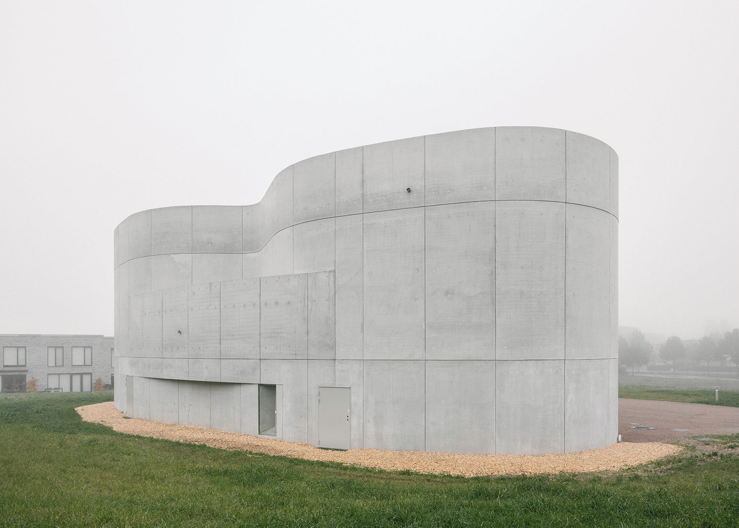 Trekroner Church by Rørbæk and Møller — Trekroner Church presents a curved concrete volume set against a misty rural landscape.