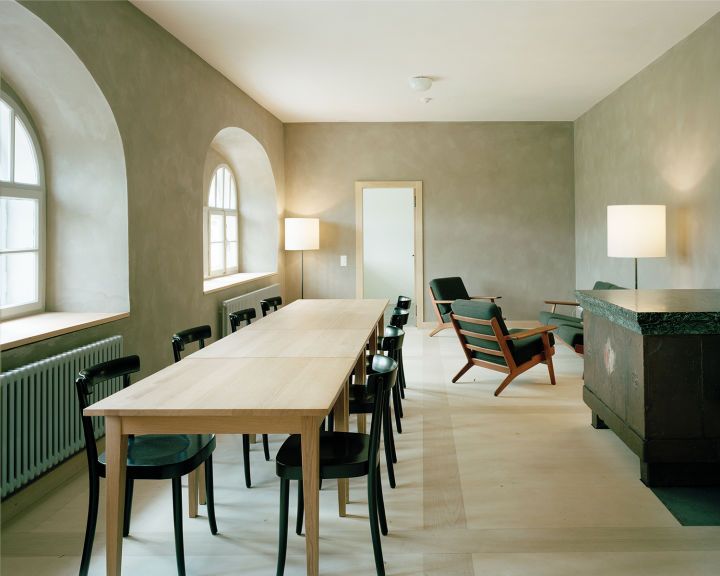 Old hospice, St. Gotthard Pass by Miller & Maranta — Interior of the renovated hospice showing a generous dining hall with a long timber table and black bentwood chairs arranged in the foreground.